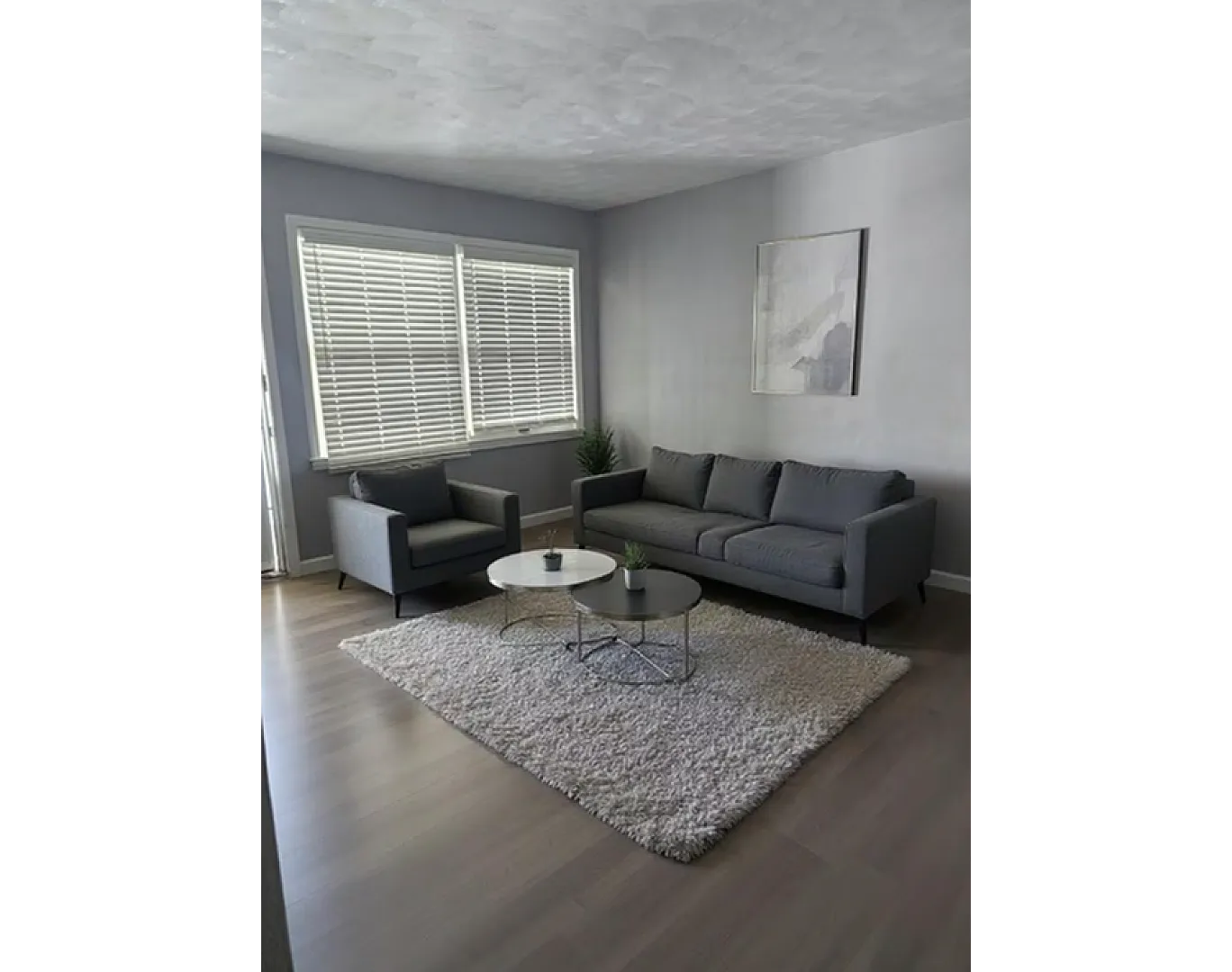 Chic living room featuring modern gray sofa set, stylish coffee tables, and large bright windows, all on a sleek wooden floor.