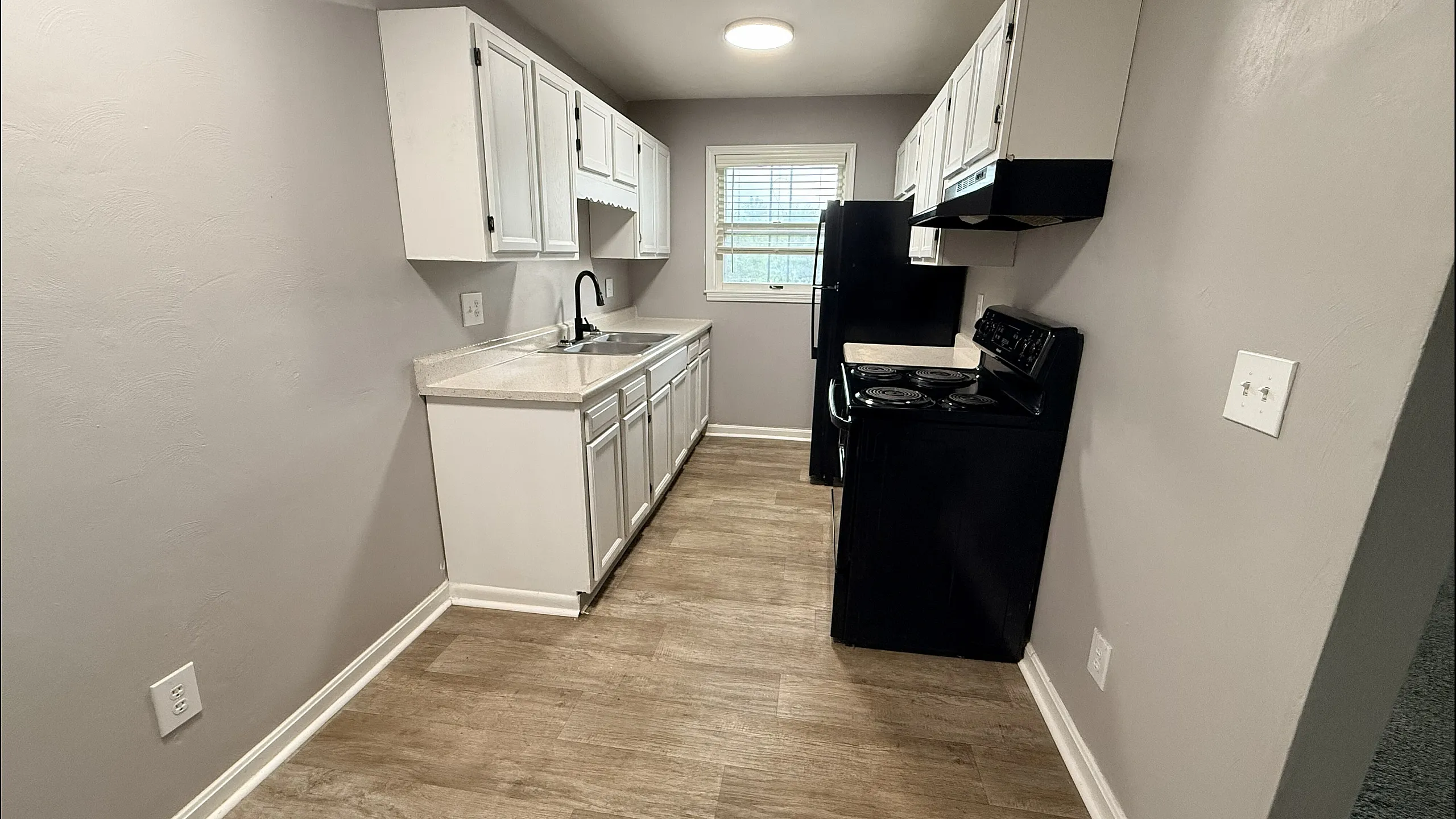 Modern apartment kitchen featuring sleek white cabinetry, stylish countertops, and a contemporary black stove with a window providing natural light.