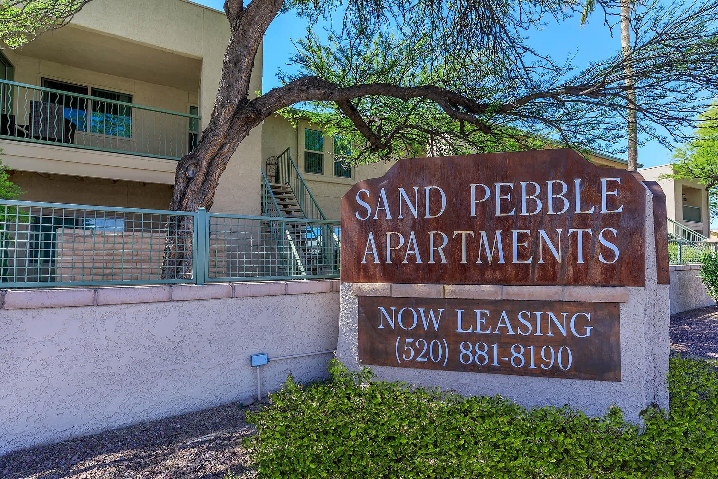 Charming Sand Pebble Apartments with inviting exterior, lush greenery, and modern amenities, now leasing.
