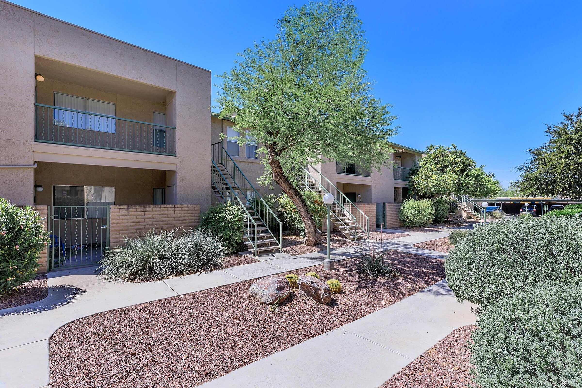 Charming apartment complex with lush landscaping, featuring desert plants and spacious balconies, under a clear blue sky.