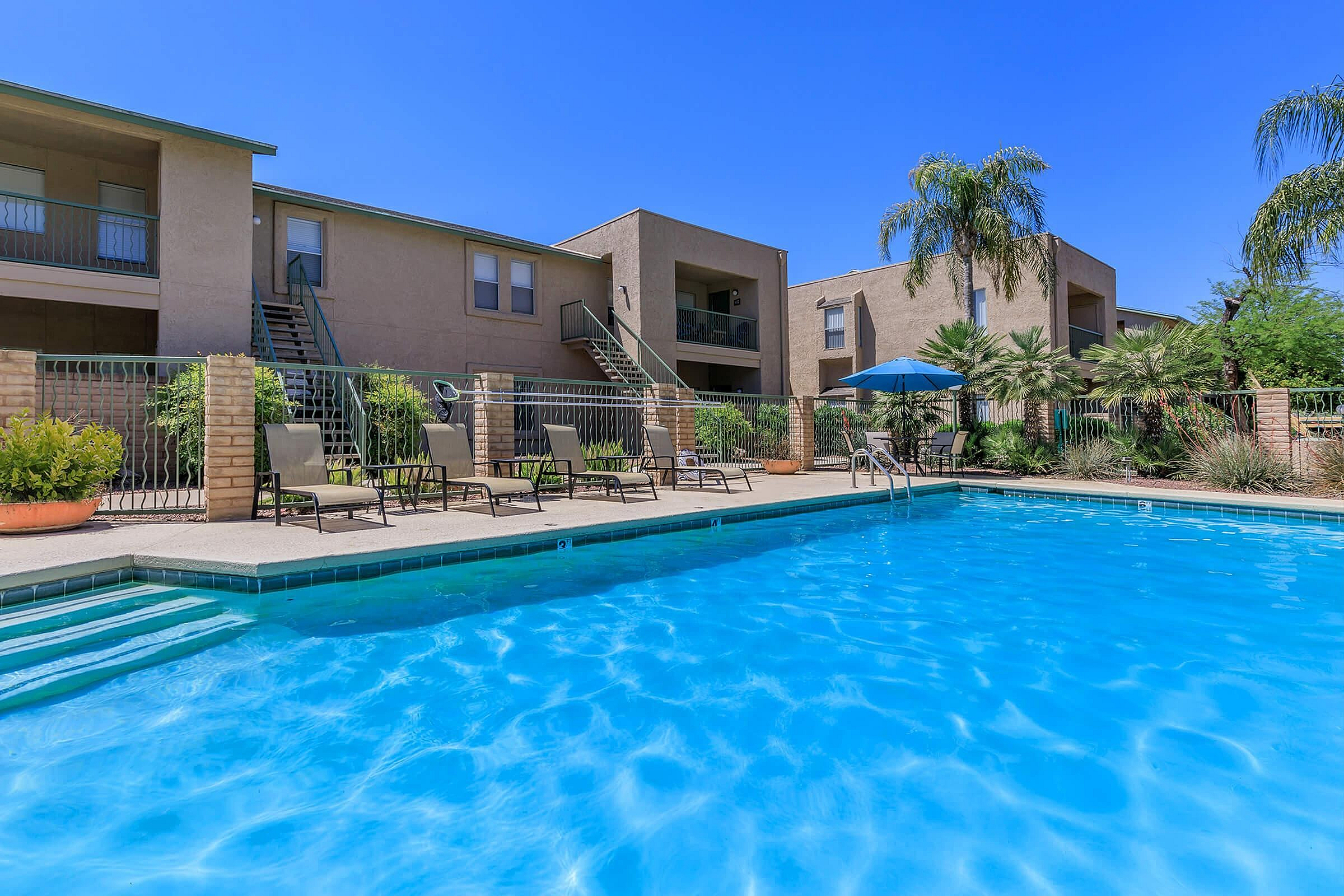 Inviting apartment complex featuring a sparkling outdoor pool with sun loungers and lush palm trees, perfect for enjoyable relaxation and leisure.
