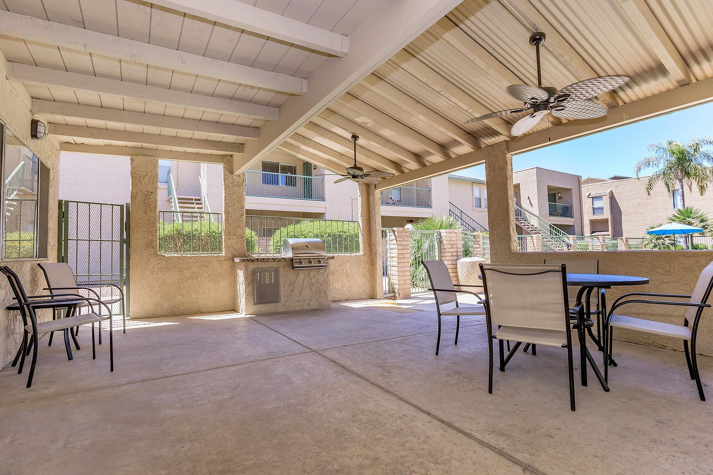 Inviting covered patio area with modern outdoor seating and built-in BBQ grill, perfect for entertaining or relaxing in a sunny apartment complex.