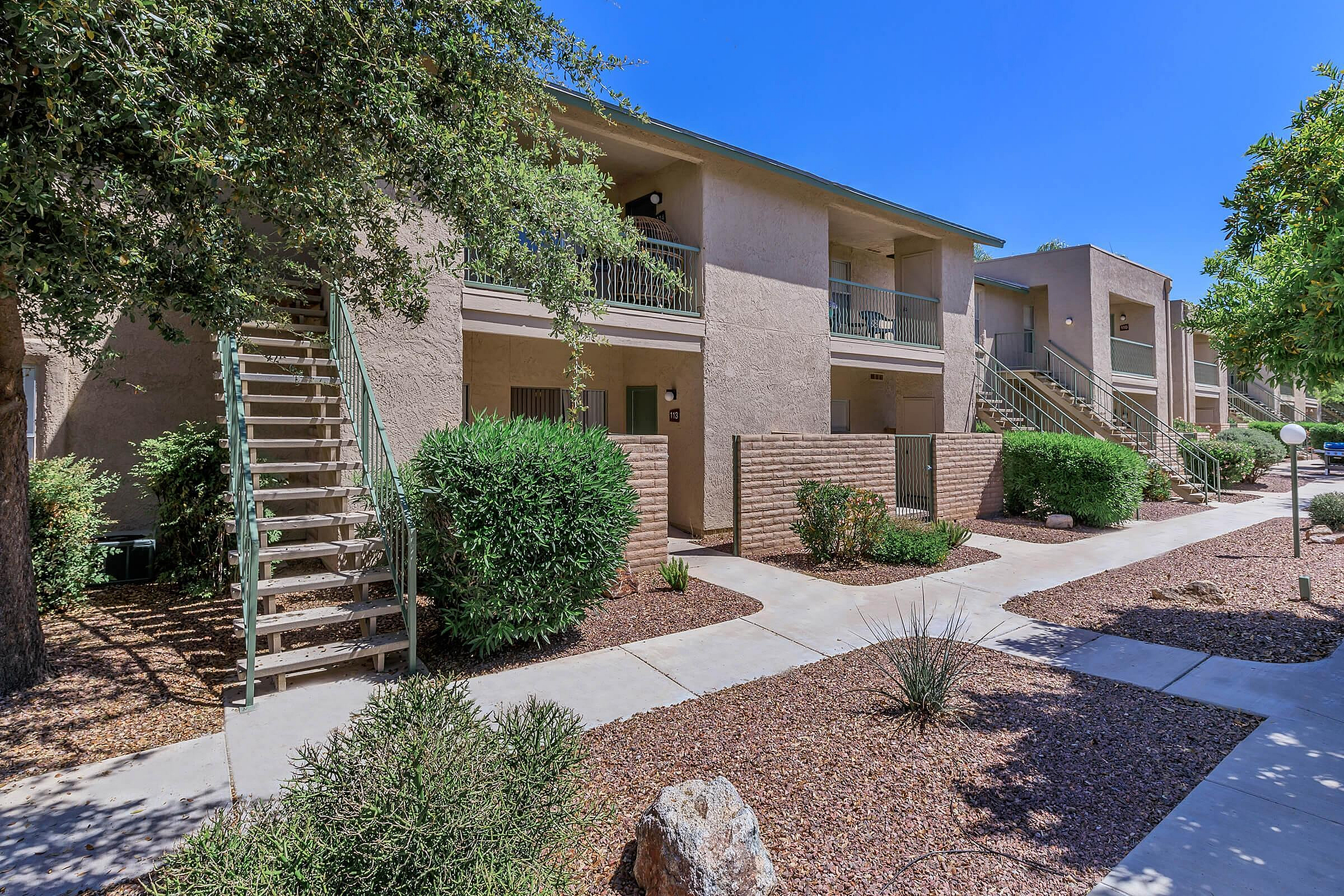 Charming apartment exterior showcasing lush landscaping, private patios, and inviting staircases leading to cozy entrances.
