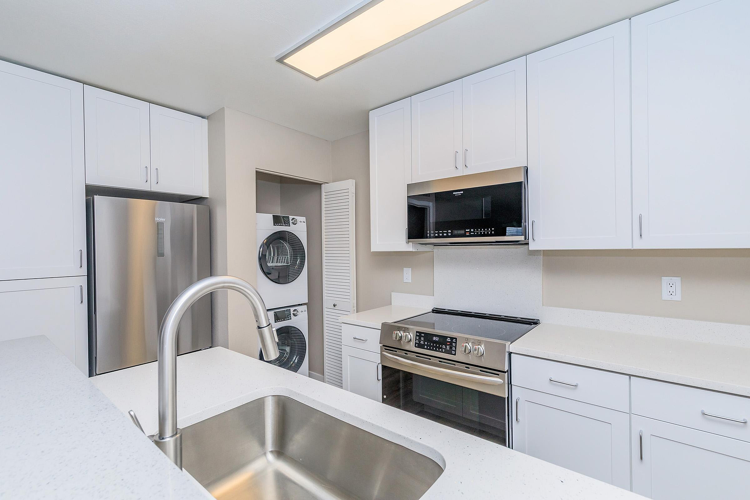Modern kitchen with sleek white cabinetry, stainless steel appliances, and a convenient in-unit washer and dryer.