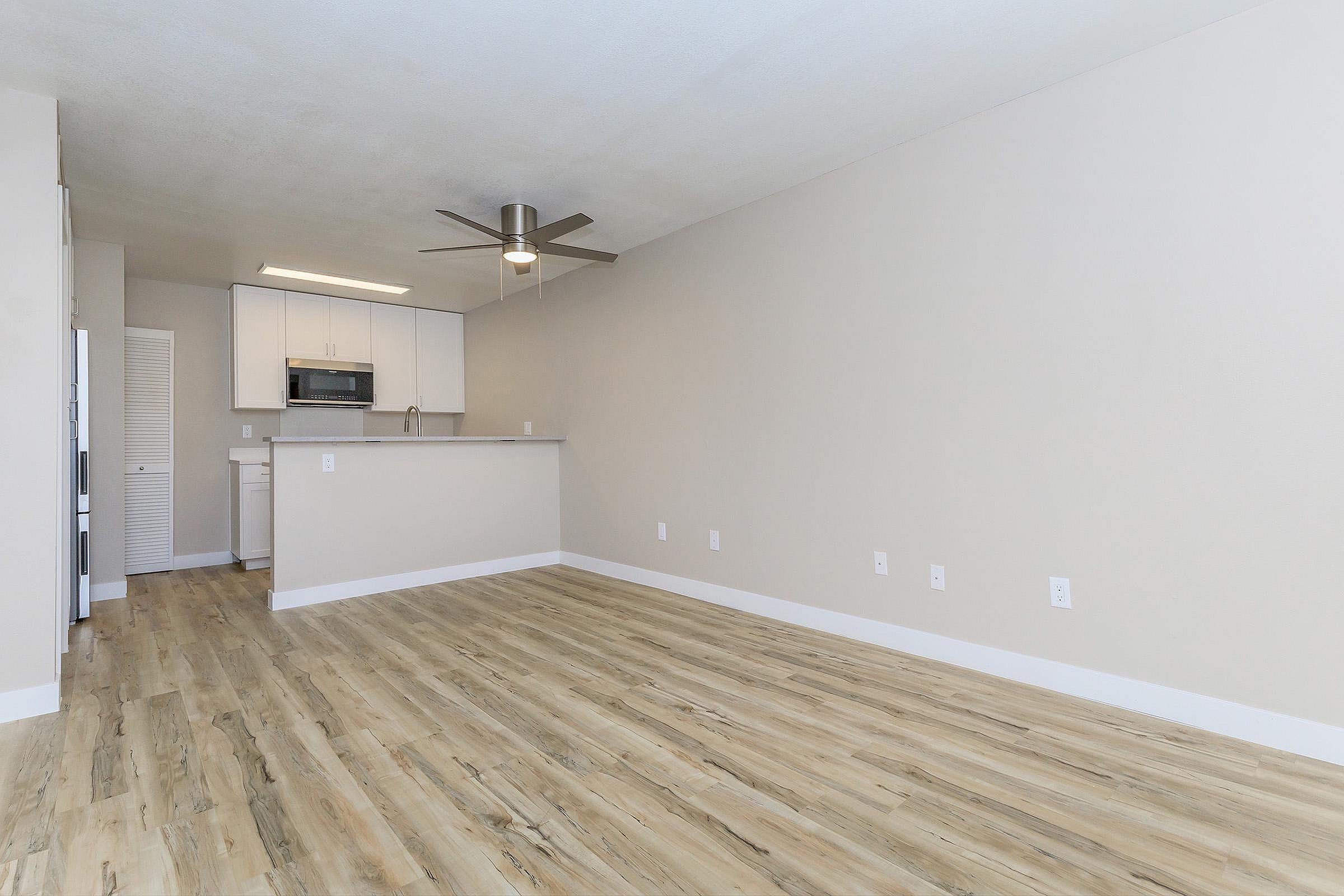 Bright open-concept living area with modern kitchen, sleek ceiling fan, and elegant wood flooring.
