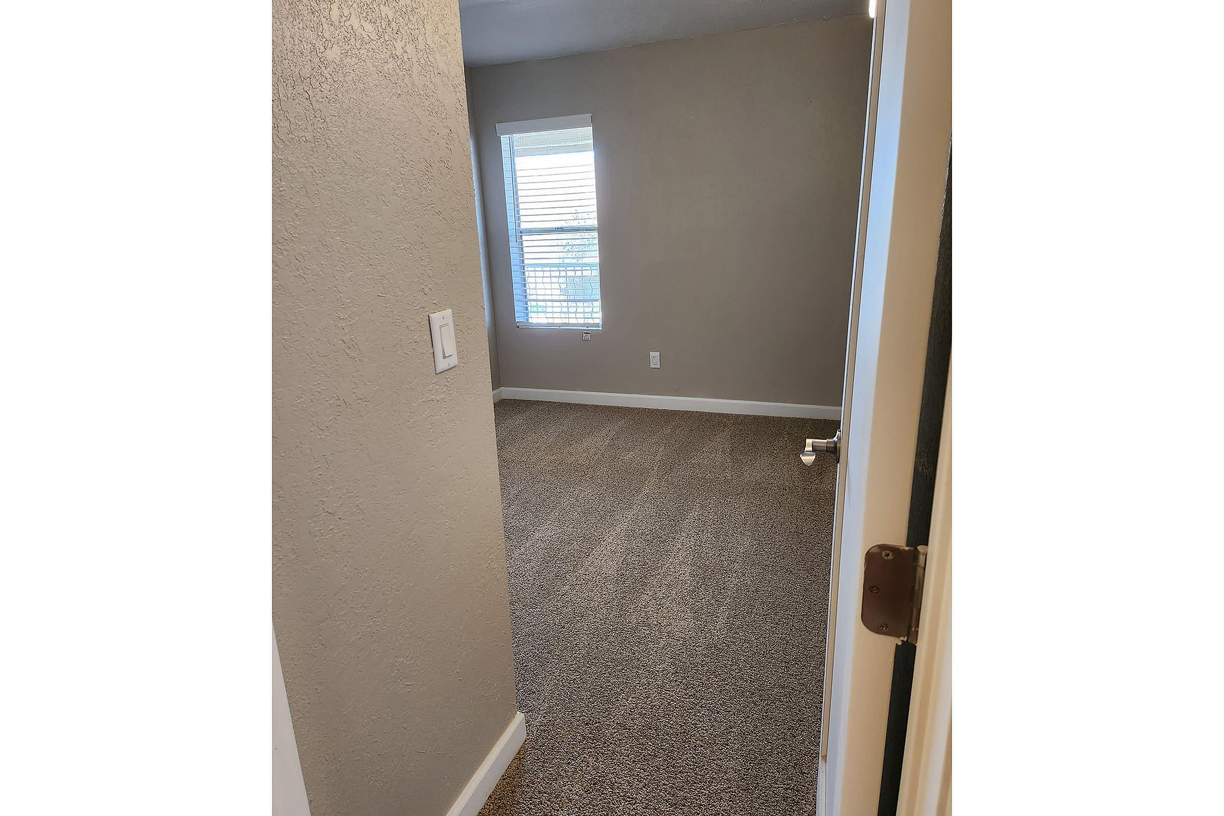 Inviting room with plush carpeting, a soft neutral color palette, and a large window letting in natural light.