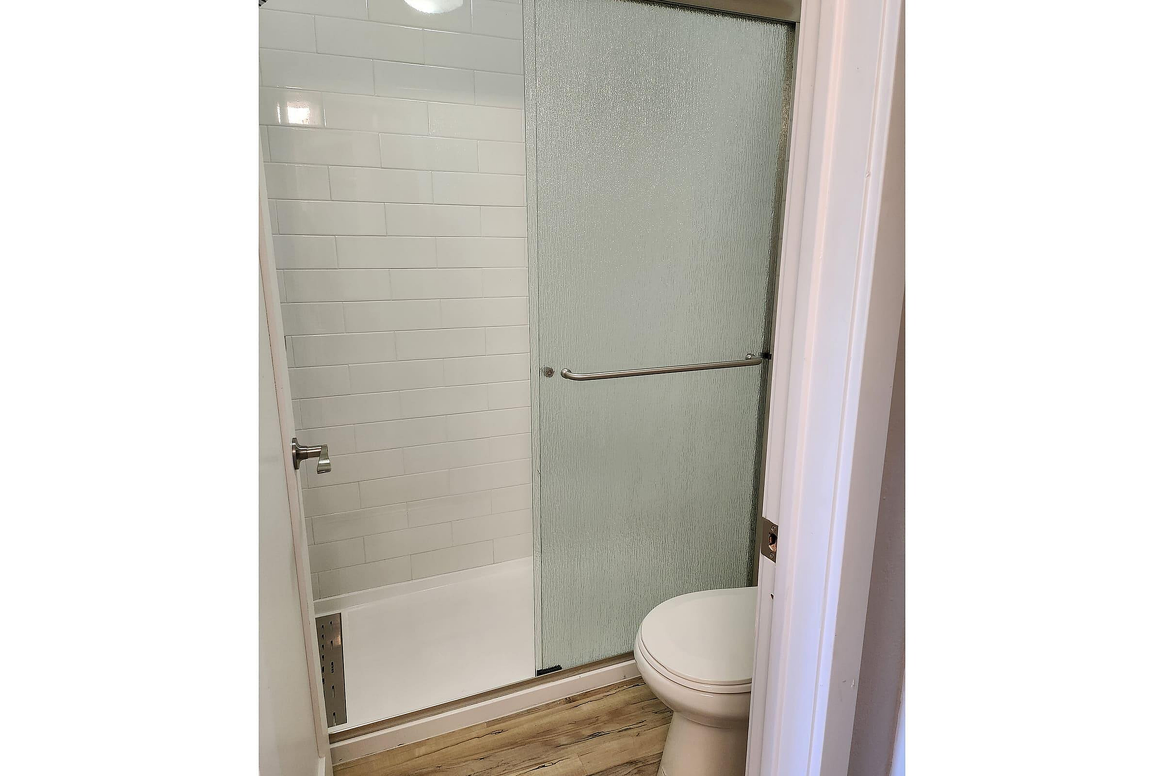 Modern bathroom with sleek glass shower door, elegant tile walls, and stylish wood-look flooring.