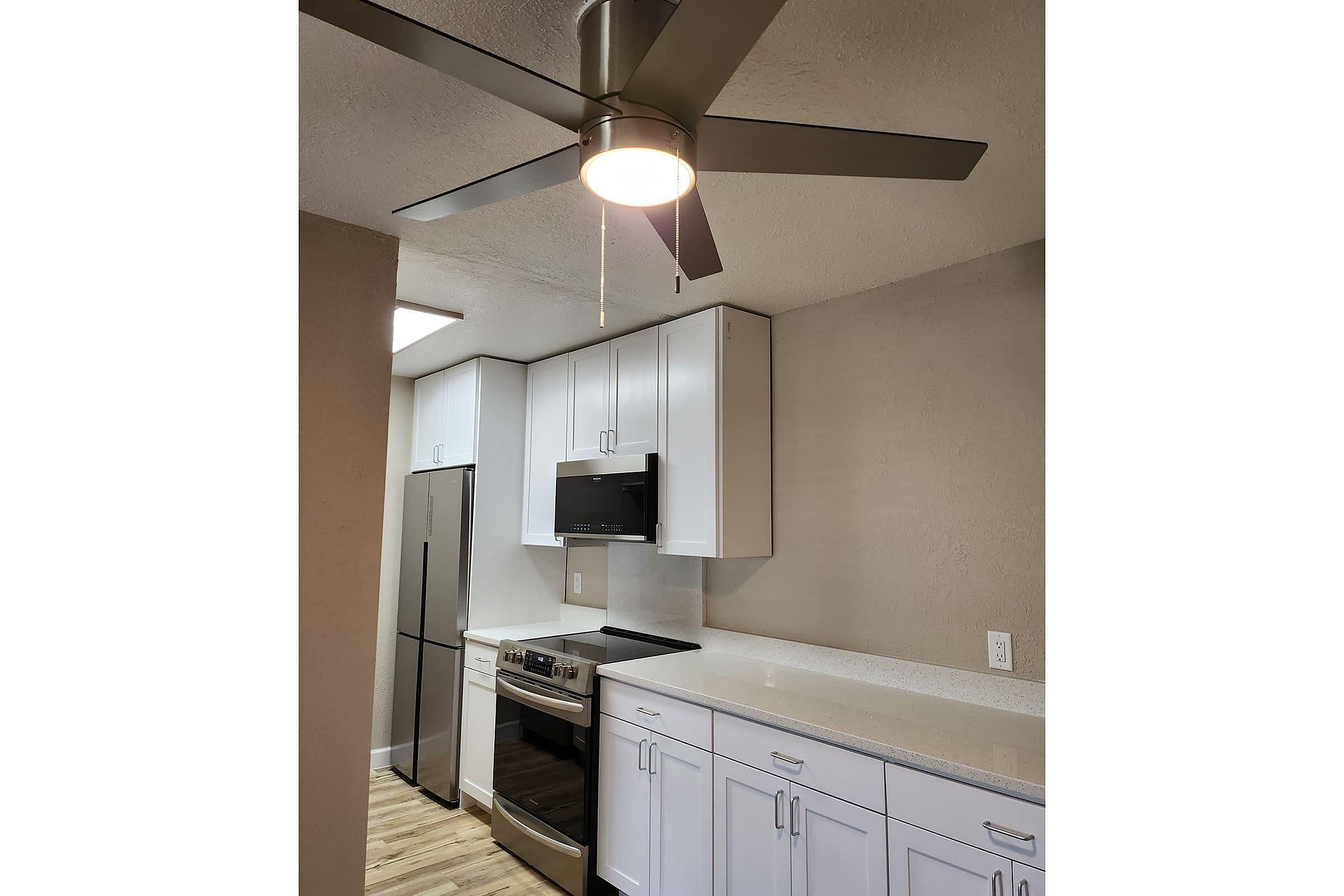 Modern kitchen with sleek stainless steel appliances, elegant white cabinetry, and a stylish ceiling fan.