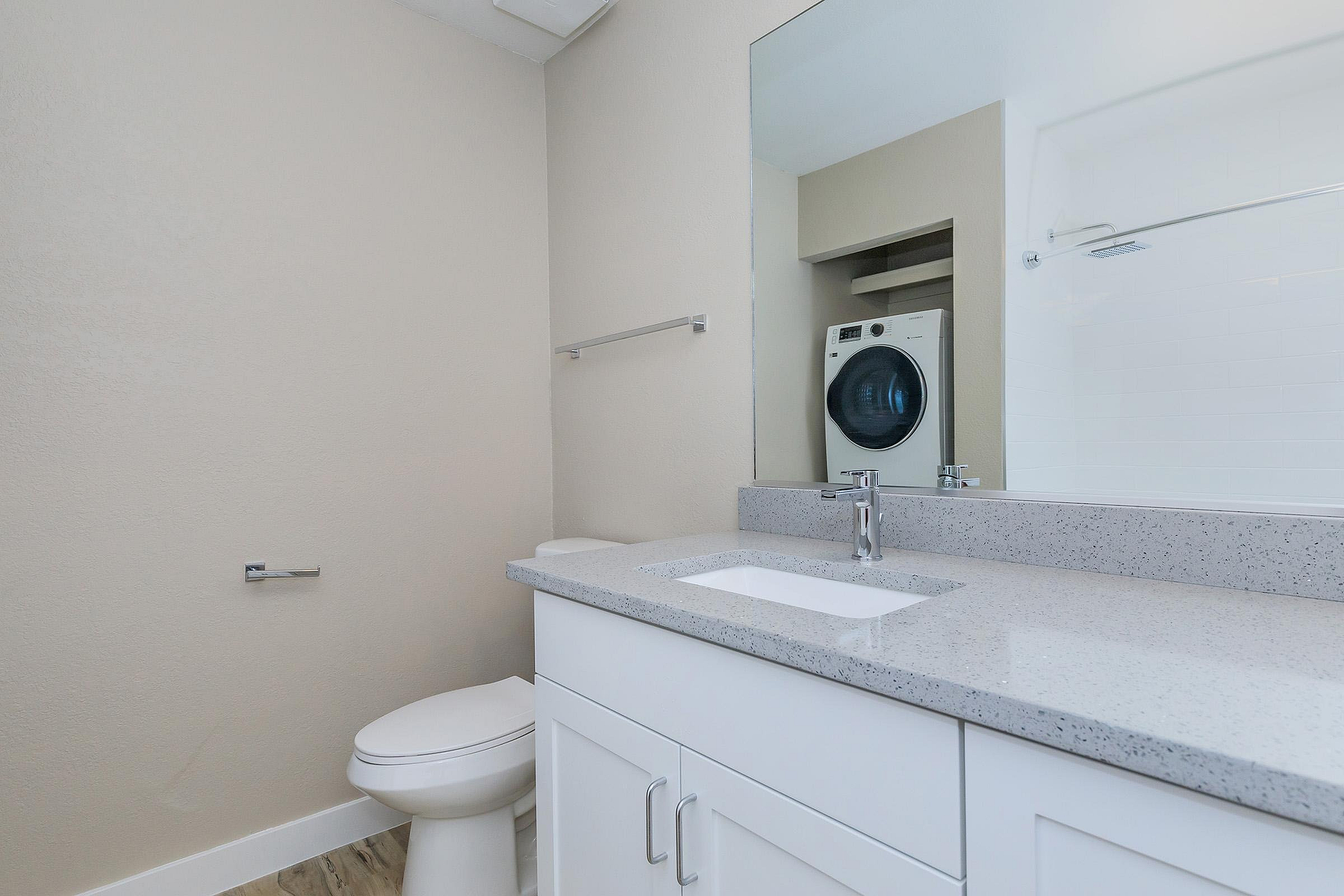 Sleek and modern bathroom with quartz countertop, washer and dryer unit, and a spacious mirror.