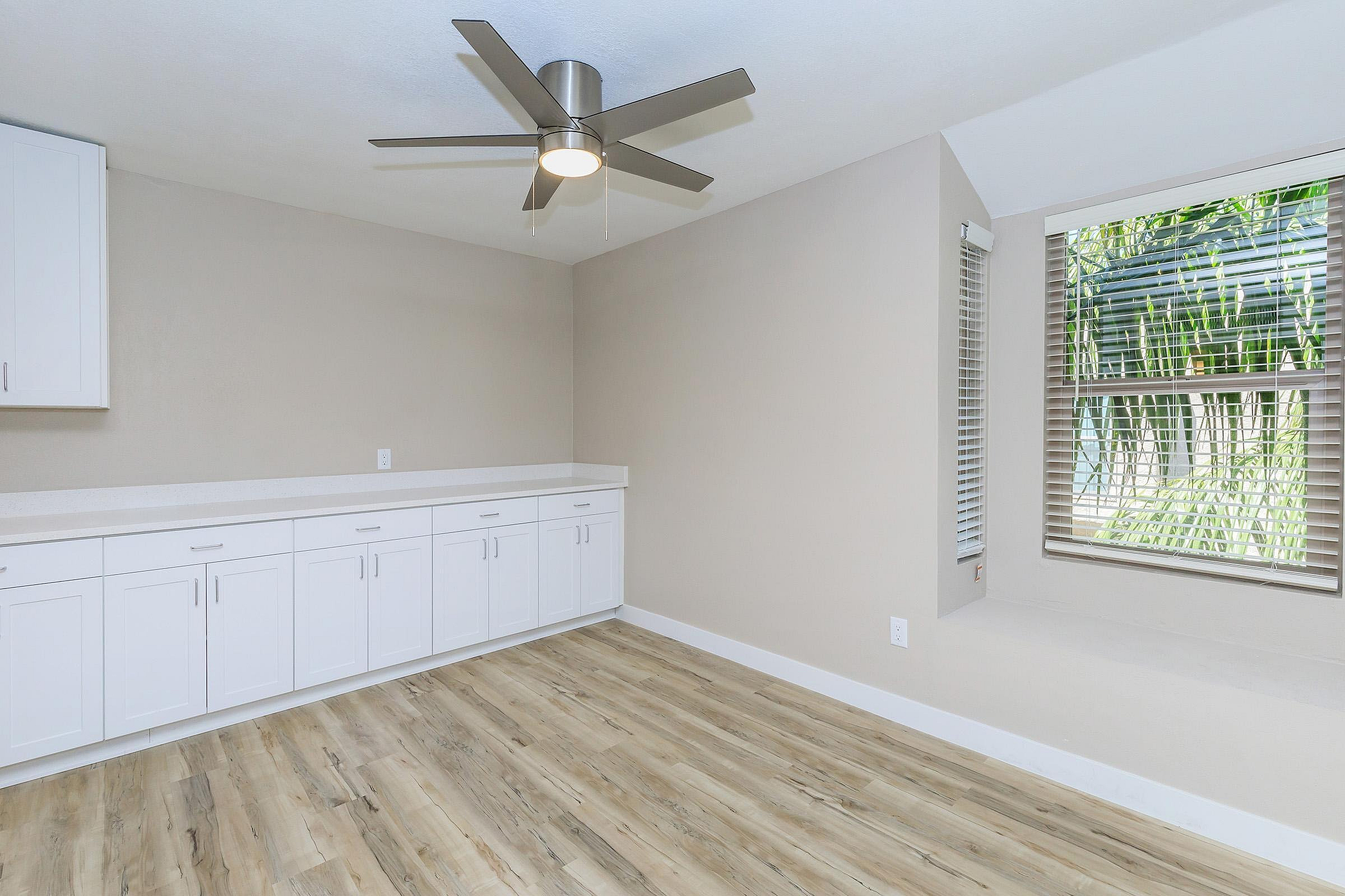 Bright and modern room with elegant white cabinetry, sleek ceiling fan, and large window offering lush garden views, perfect for a serene living space.