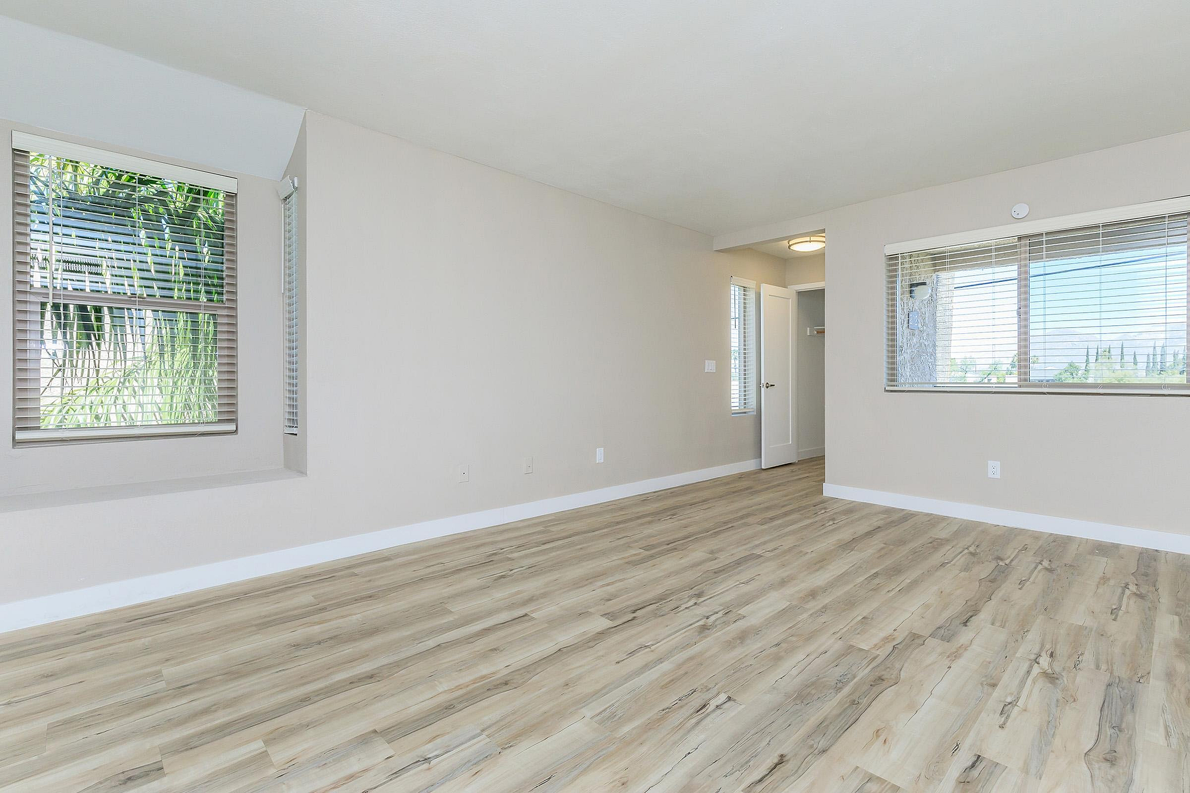Bright and spacious empty room featuring elegant hardwood floors and large windows with scenic outdoor views.