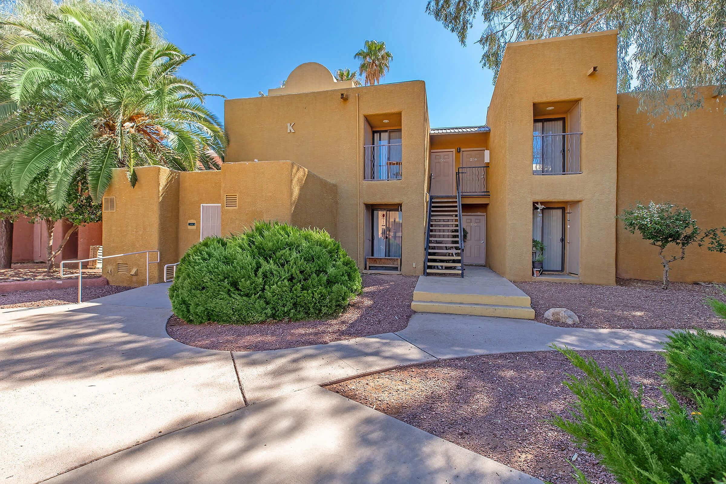 Inviting apartment building with a stunning desert landscape, featuring an attractive palm tree and elegant entryway stairs.