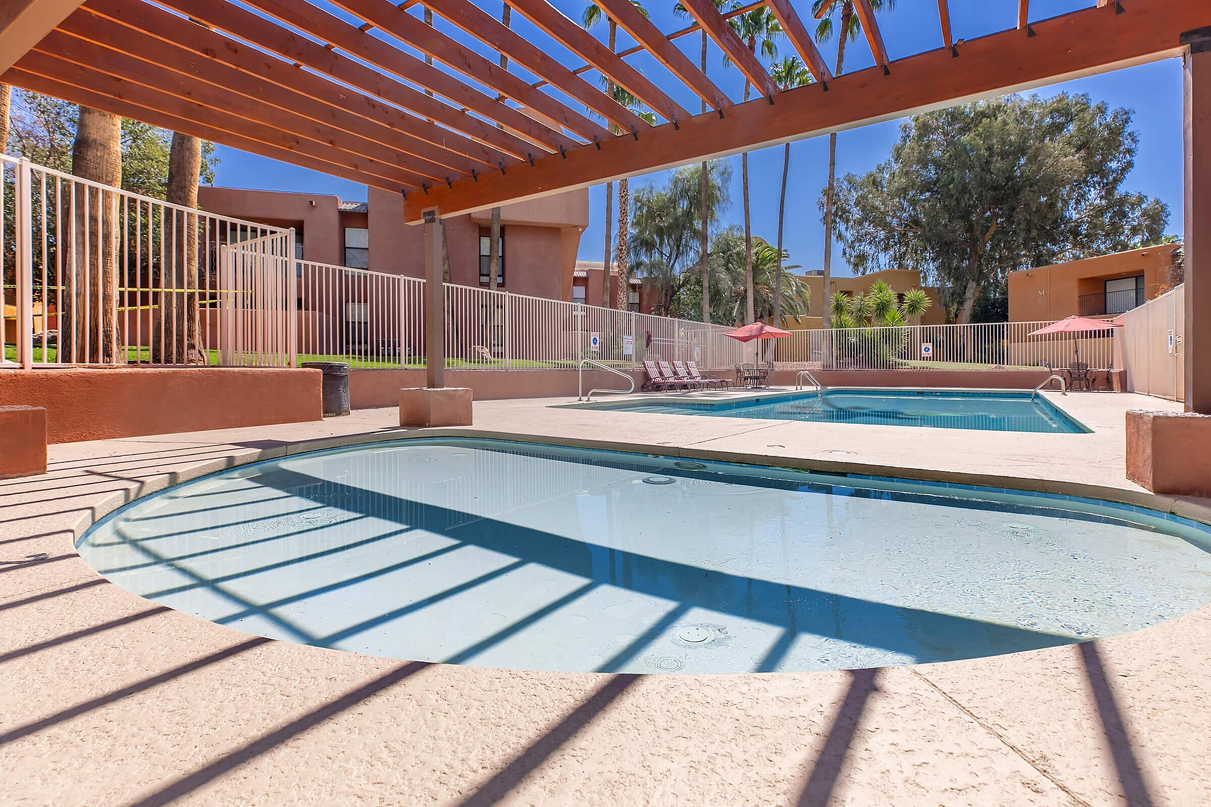 Inviting community pool area with stylish pergola and sunlit patio, perfect for relaxation and leisure.