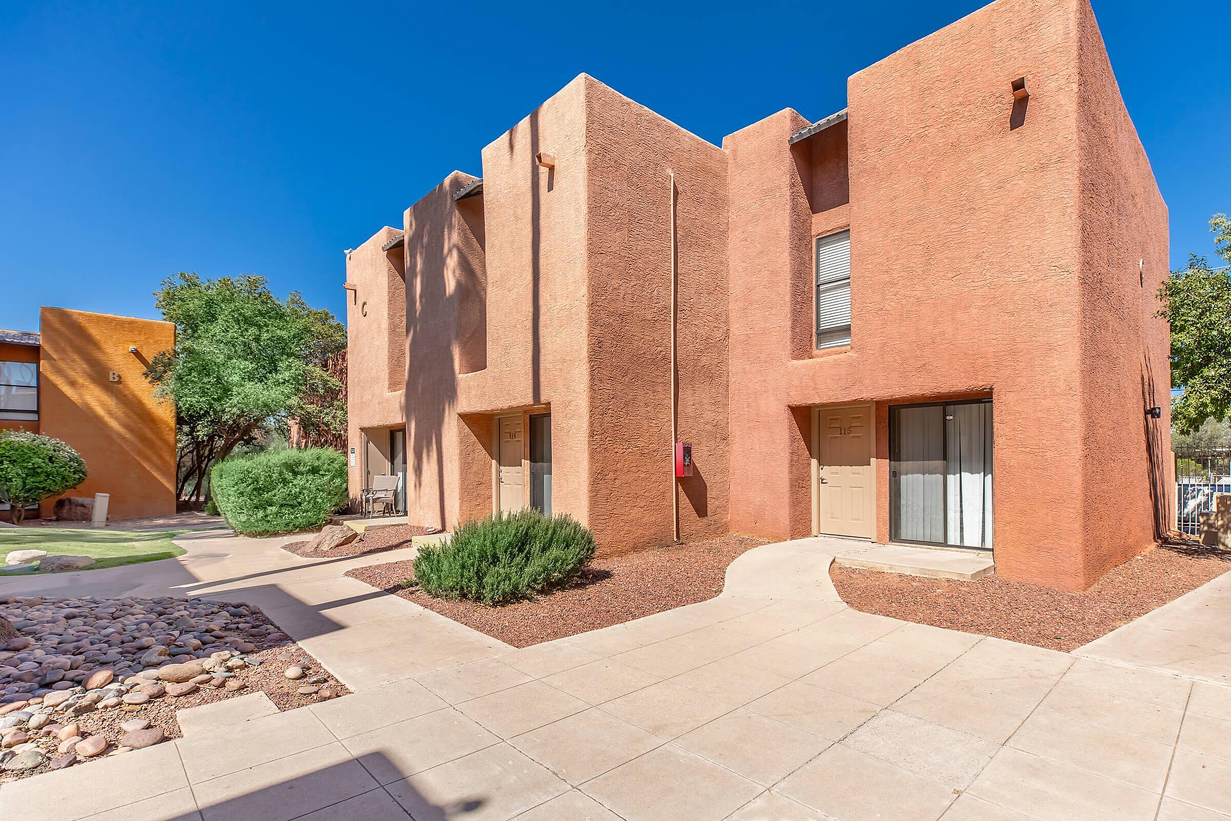 Charming desert-style duplex with rustic adobe exterior, nestled amidst lush greenery and vibrant landscaping.
