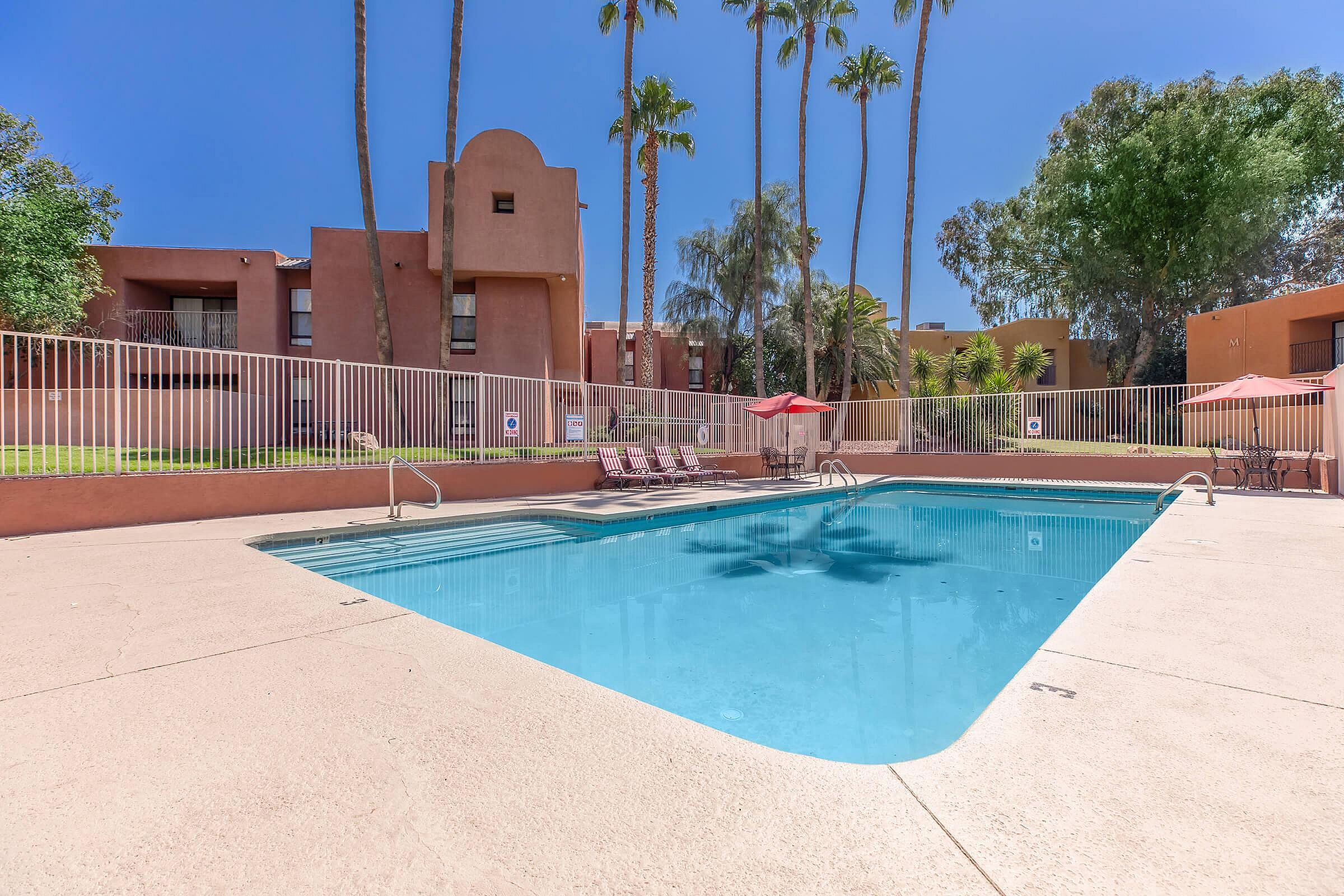 Inviting outdoor swimming pool with lounge chairs and umbrellas, surrounded by lush greenery and modern apartment buildings.