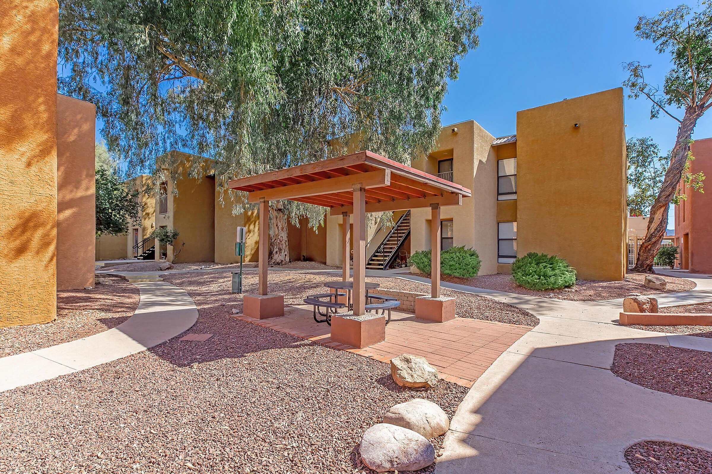 Charming apartment complex courtyard featuring a shaded picnic area surrounded by lush greenery and modern architectural design.
