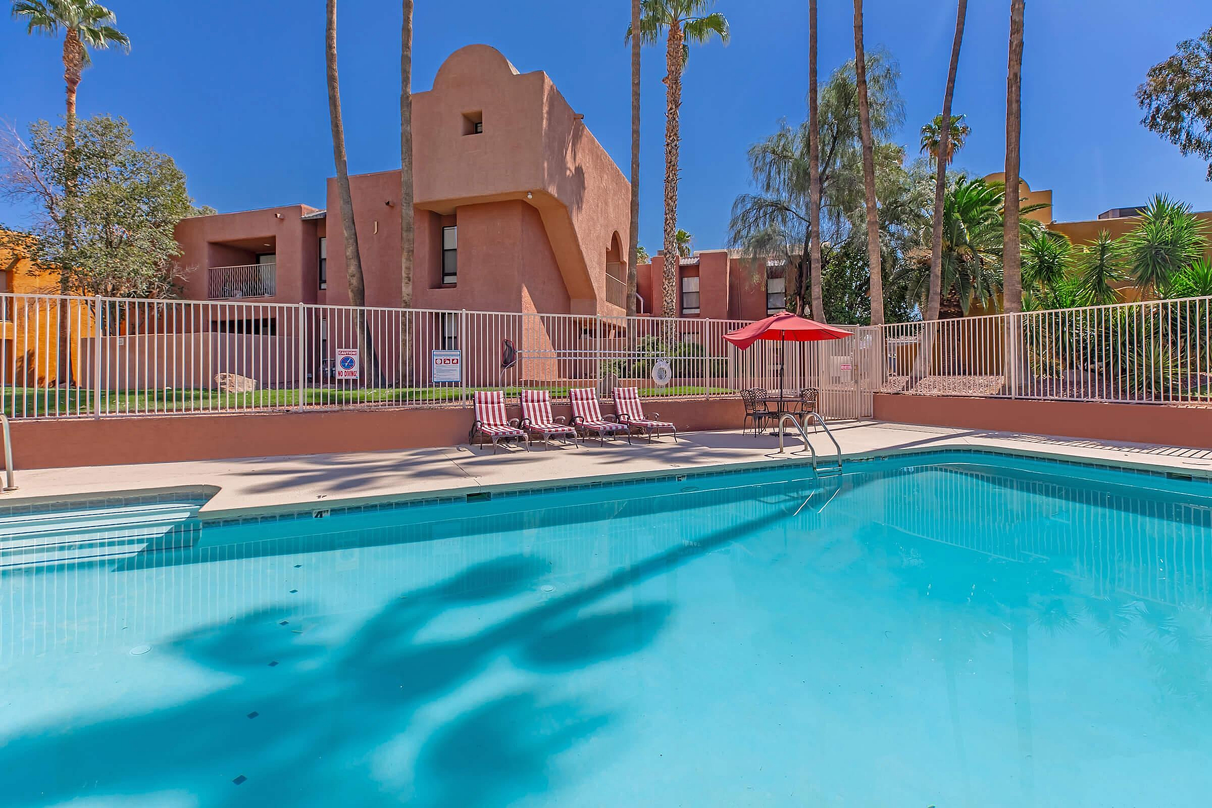 Vibrant apartment complex with a sparkling pool, surrounded by lush palm trees and inviting sun loungers.