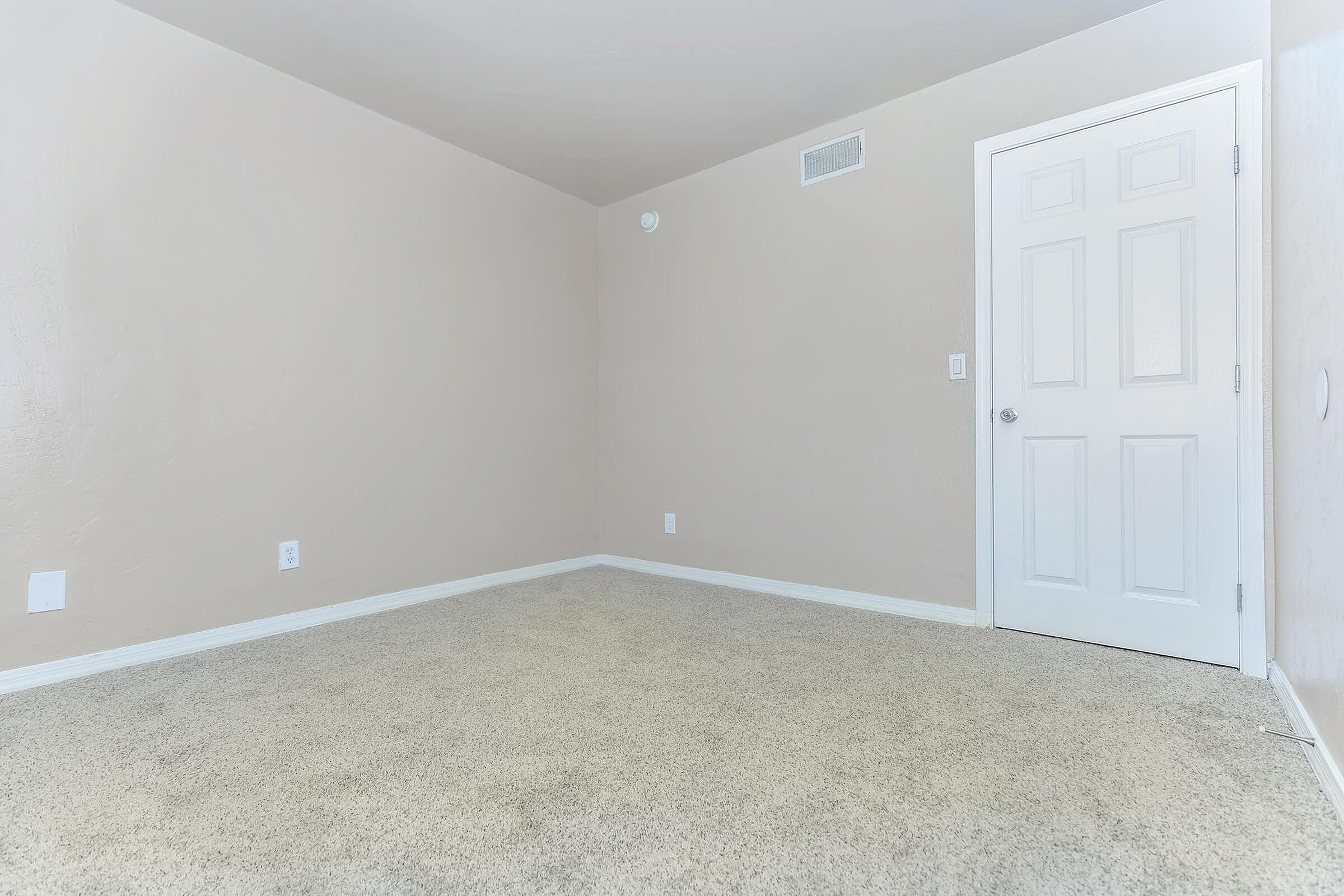 Bright, spacious room with fresh beige walls, plush carpeting, and a pristine white door, perfect for customization.