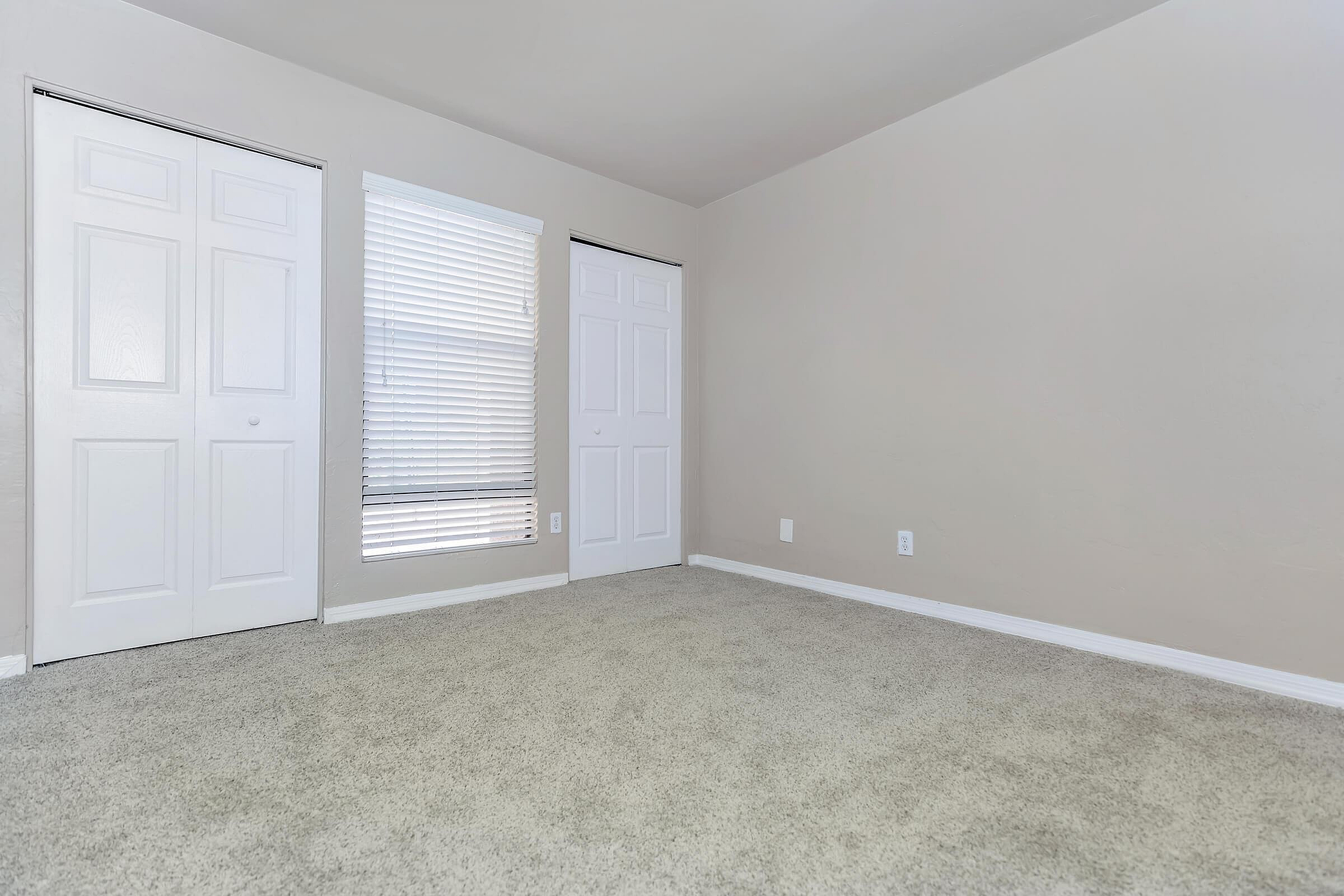 Inviting bedroom with plush carpet, dual-door closet, and natural light filtering through wide window blinds.