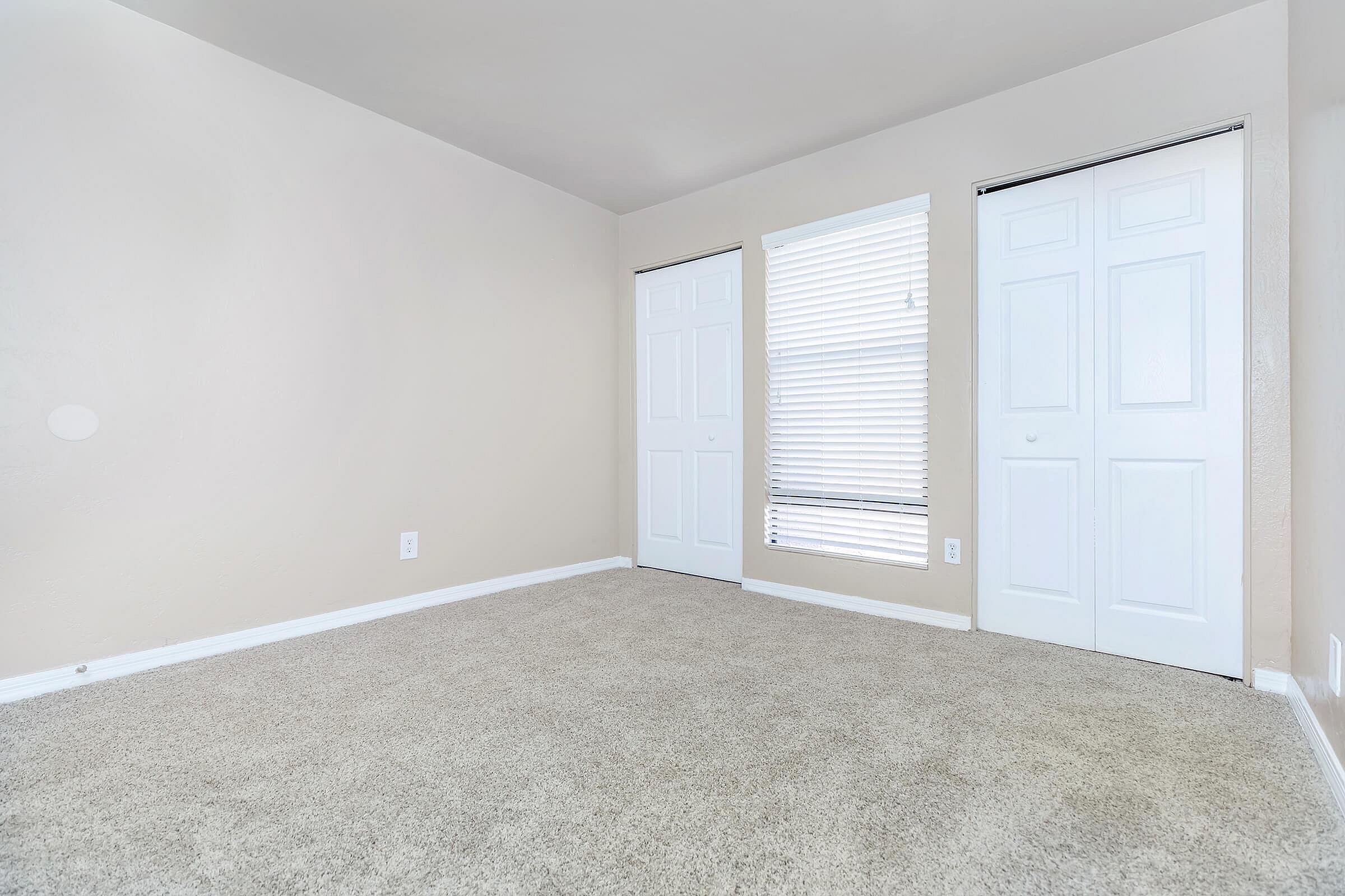 Bright and spacious bedroom with soft carpet flooring, neutral walls, and ample closet space featuring sleek white doors.