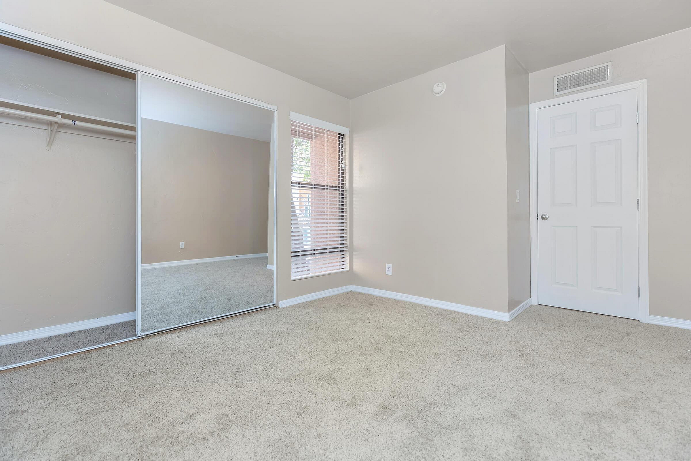 Bright and airy bedroom featuring plush carpeting, mirrored closet doors, and a large window with blinds.