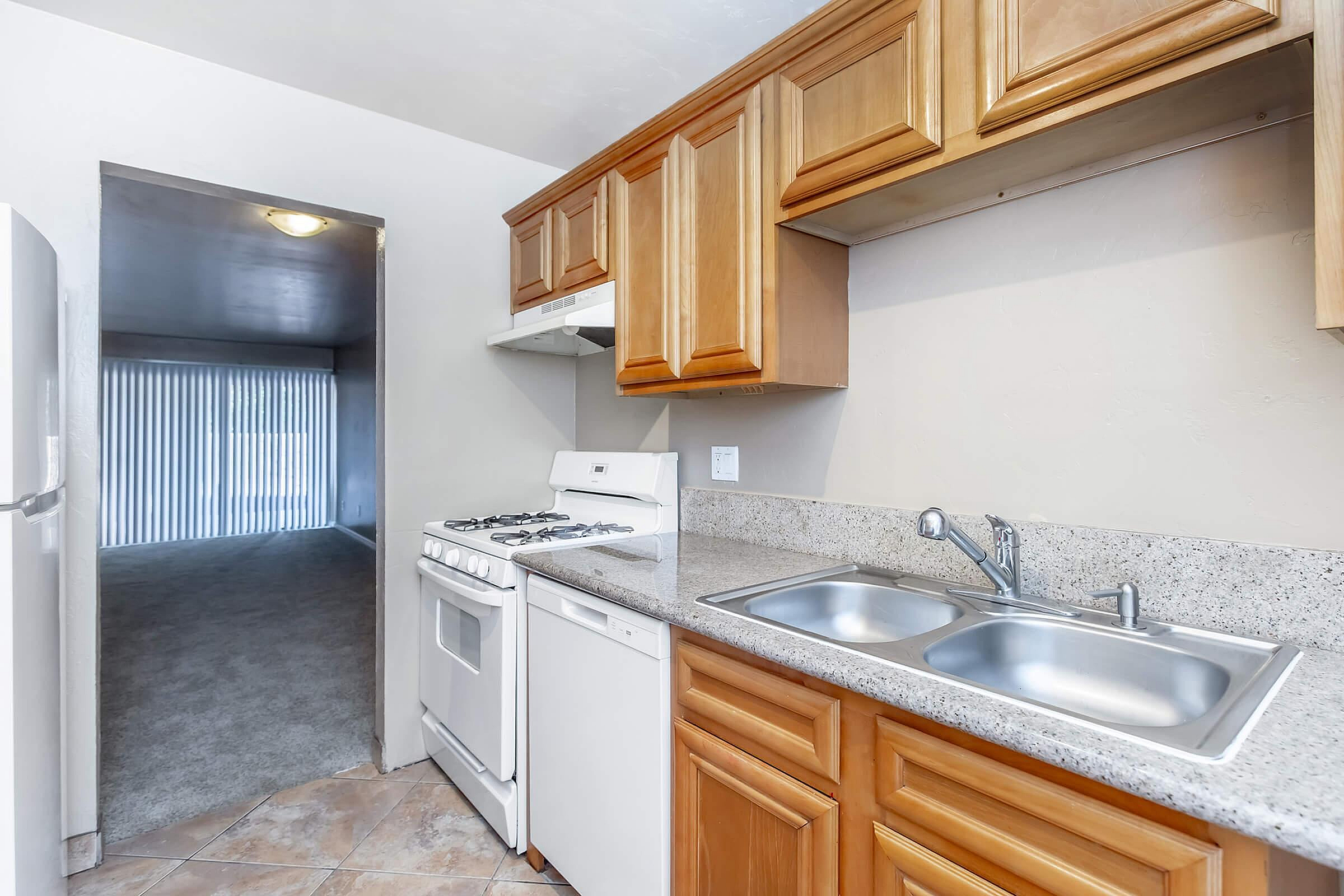 Bright and inviting kitchen with wood cabinetry, sleek granite countertops, and modern appliances, leading to a cozy living area with natural light.
