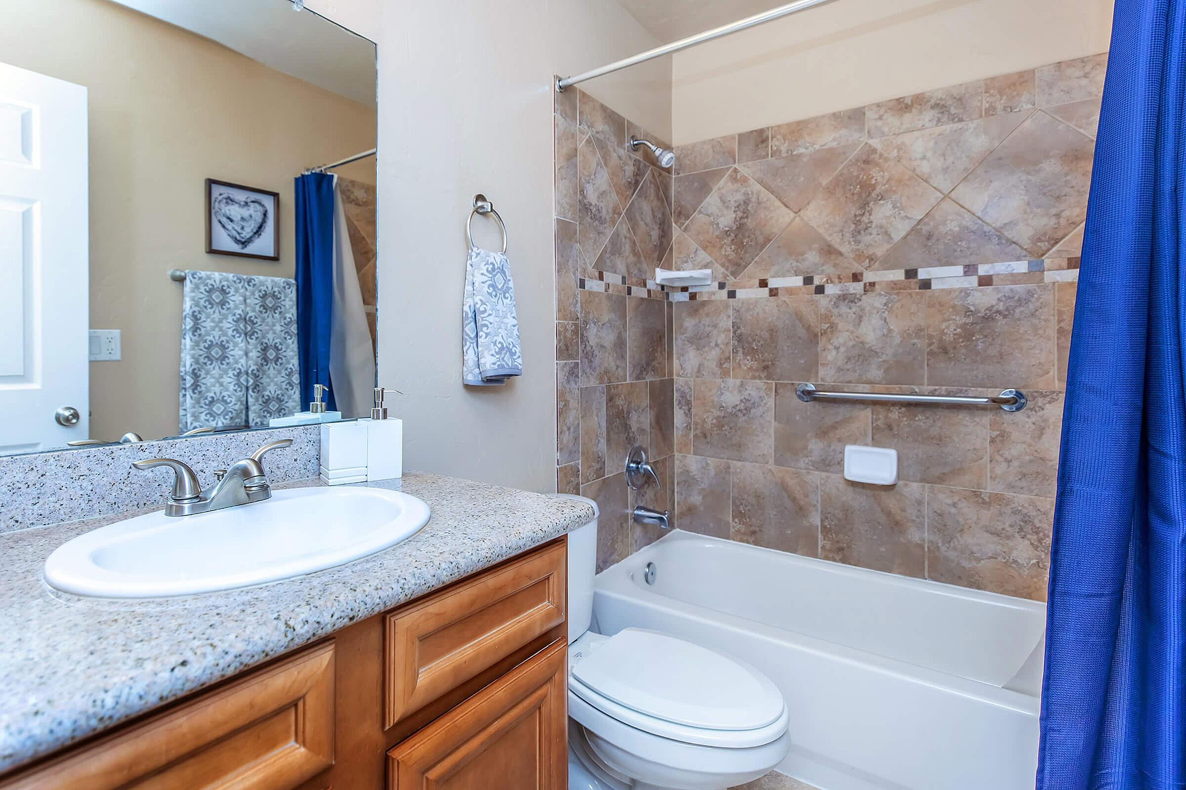 Elegant bathroom with stylish tilework, granite countertop, and polished fixtures, featuring a soothing blue shower curtain and decorative accents.