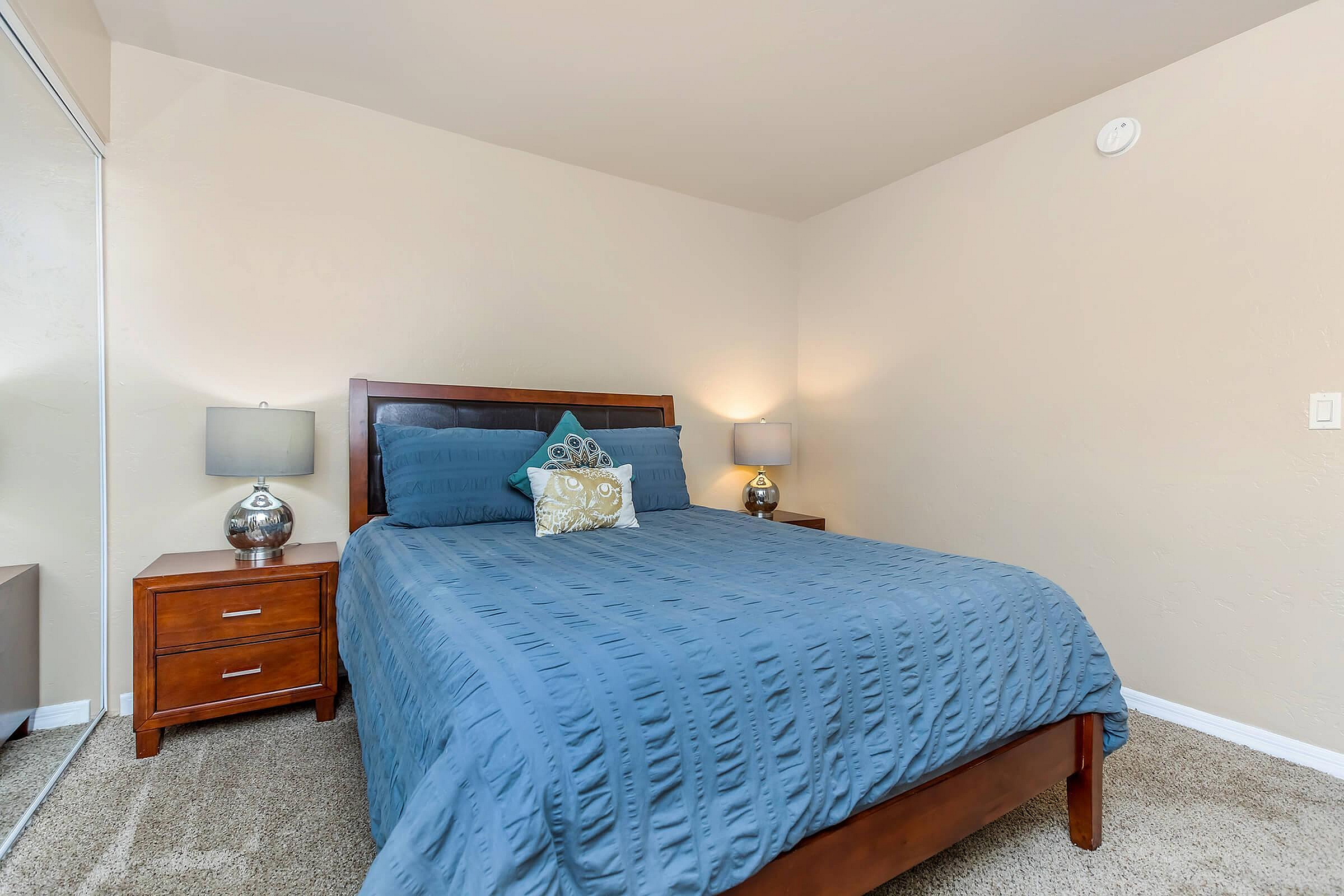 Inviting bedroom with a cozy queen bed, stylish blue bedding, and sleek wooden furniture, creating a warm and relaxing atmosphere.