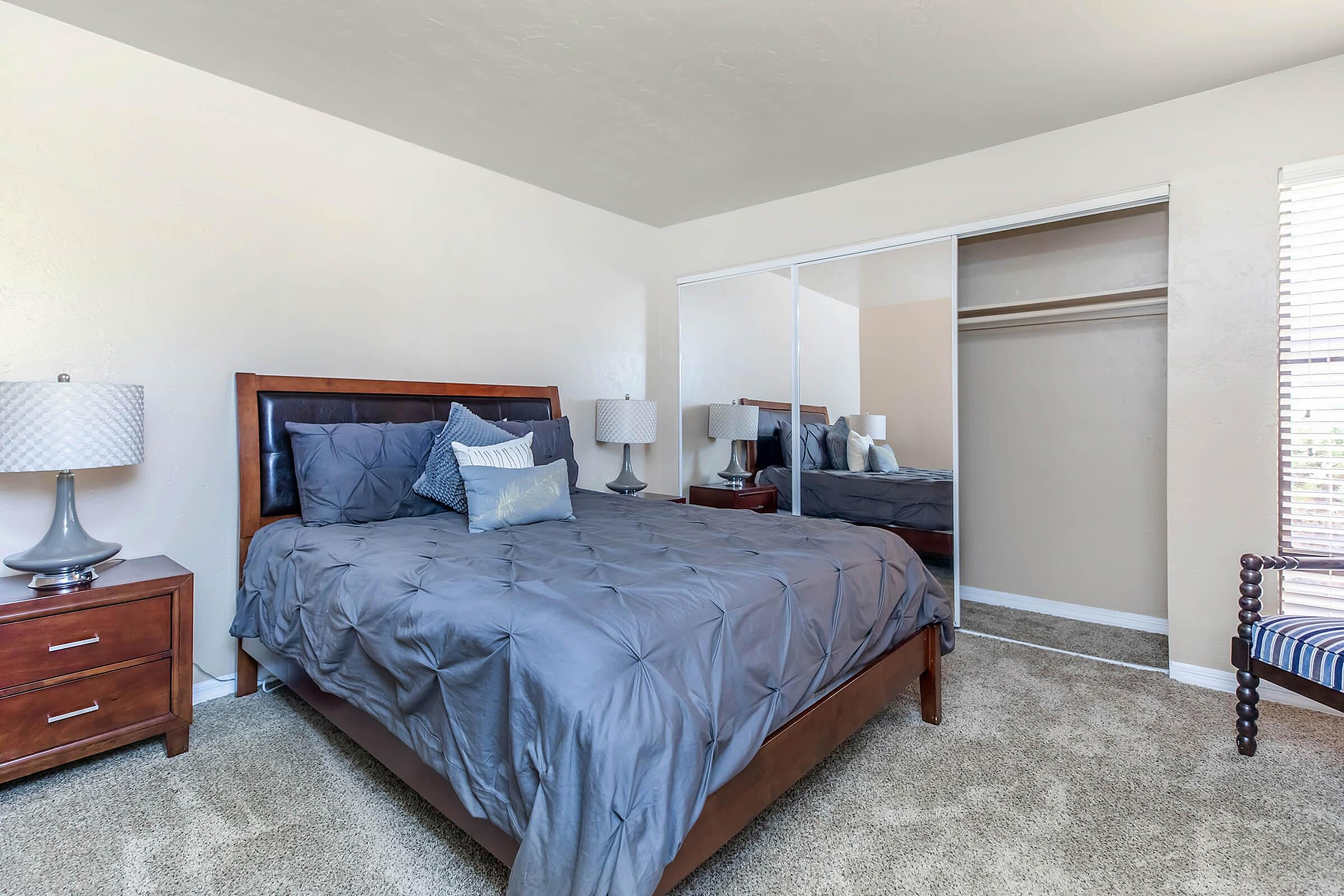 Elegant bedroom featuring a plush bed with modern navy bedding, sleek mirrored closet doors, and sophisticated bedside lamps for a cozy atmosphere.