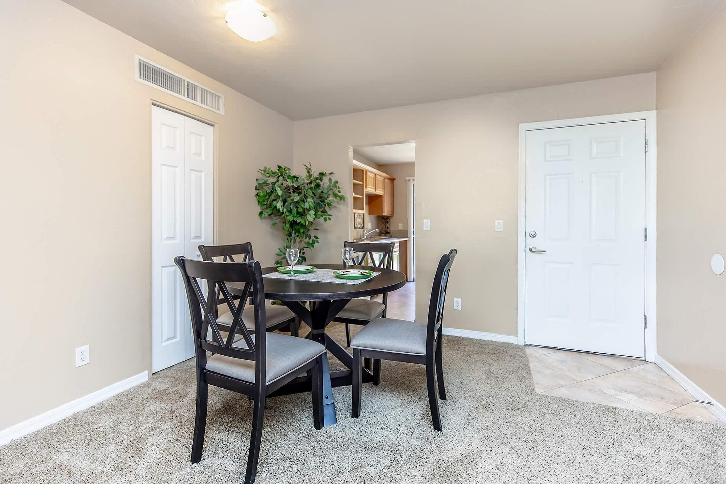 Bright dining area featuring a chic round table with stylish chairs, complemented by a lush indoor plant and cozy carpet flooring.