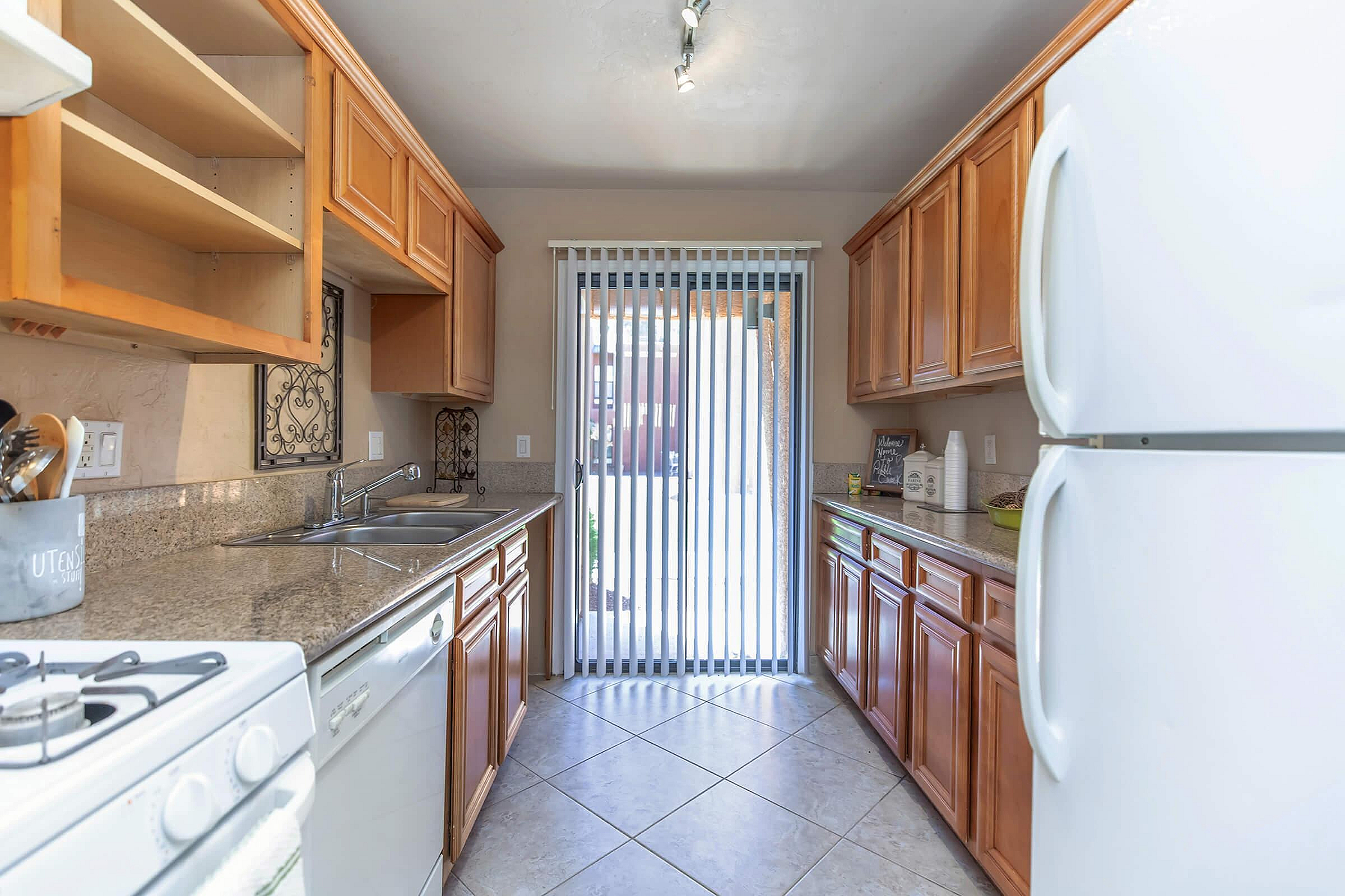 Modern kitchen with granite countertops, wooden cabinets, and large window lighting. Includes essential appliances, giving a warm and inviting feel.