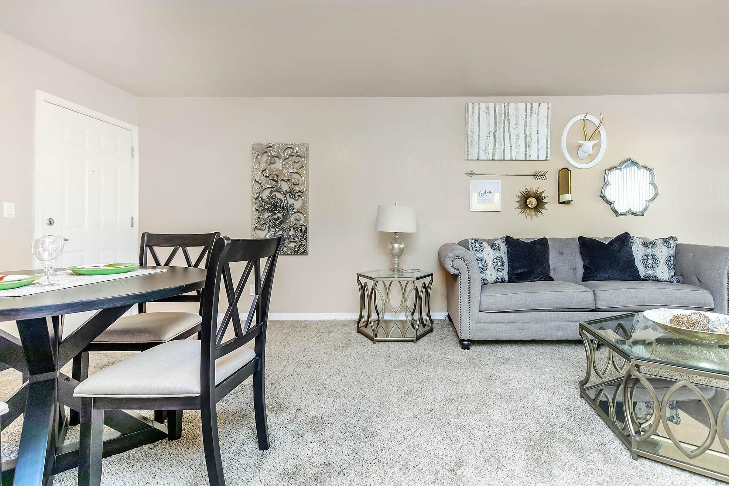 Stylish living room with a chic gray sofa, elegant glass coffee table, and modern dining area in a cozy, well-lit space.