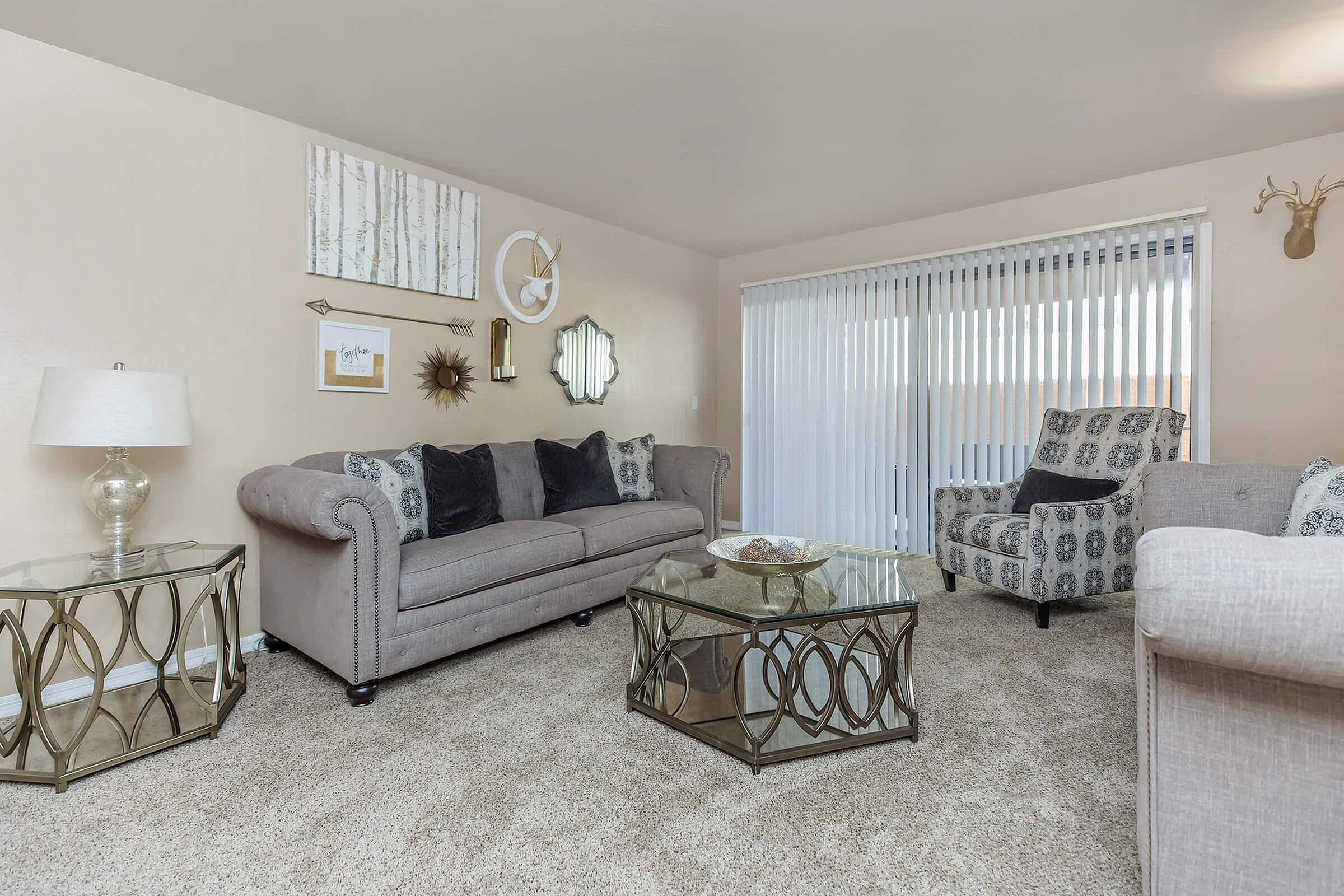 Elegant living room with stylish grey sofas, designer patterned armchair, and chic glass coffee table, enhanced by decorative wall art and cozy carpeting.