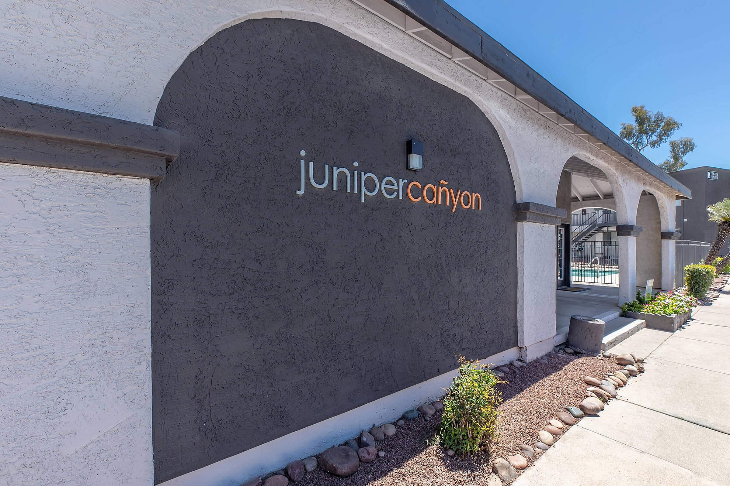 Charming entrance to Juniper Canyon apartments showcasing modern architecture with stylish arches in a serene, landscaped setting.