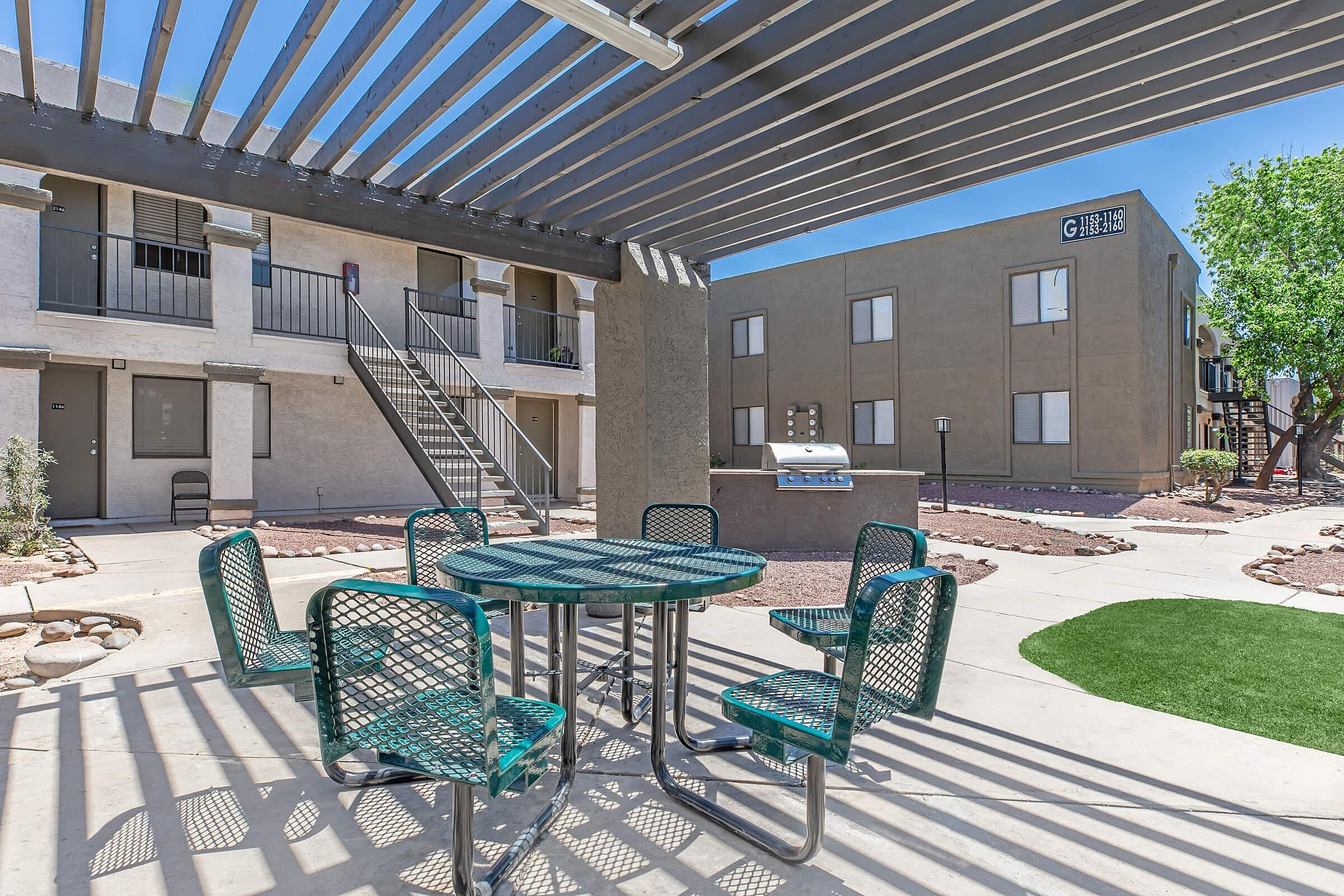 Charming outdoor patio area with stylish green seating, covered pergola, and built-in grill, perfect for gatherings in a welcoming apartment community.
