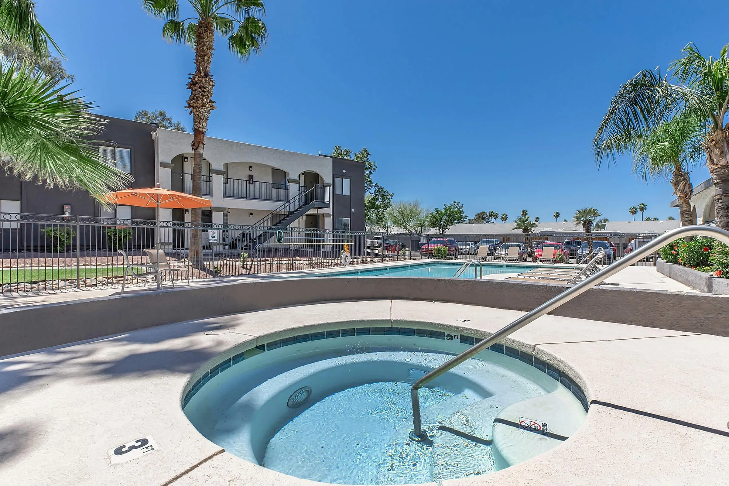 Inviting apartment complex with sunlit pool area, spa, and tropical landscaping creating a resort-like ambiance.