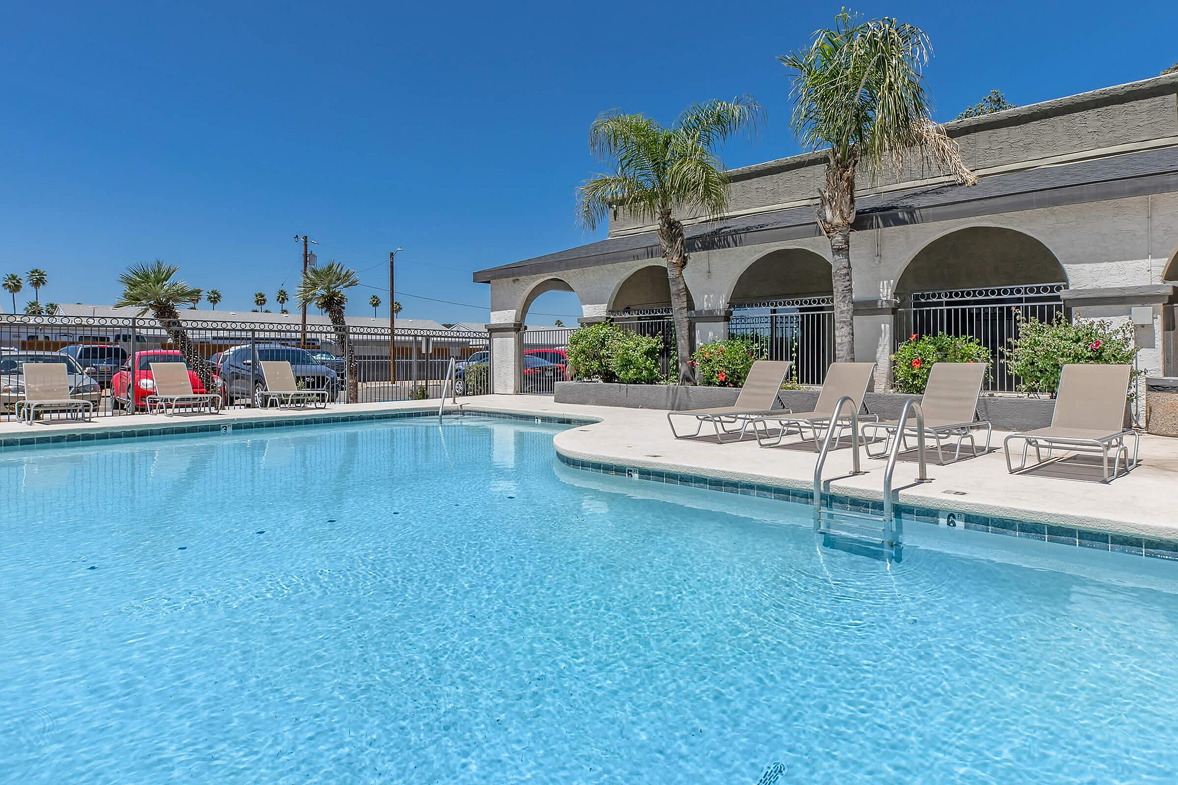 Inviting outdoor pool area with clear blue water, surrounded by stylish lounge chairs and lush palm trees under a vibrant sky.