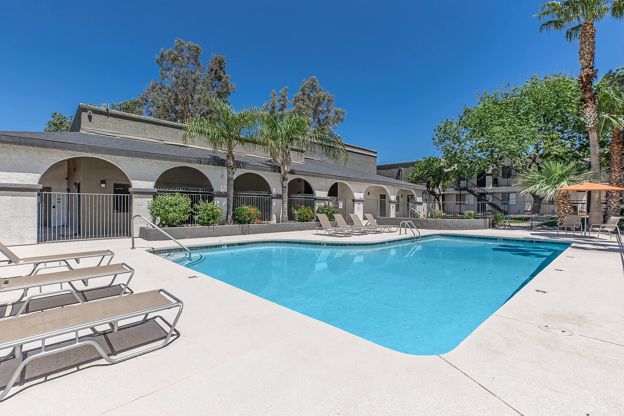 Inviting swimming pool area with sun loungers, surrounded by lush palm trees and modern architecture, perfect for relaxation and enjoyment.