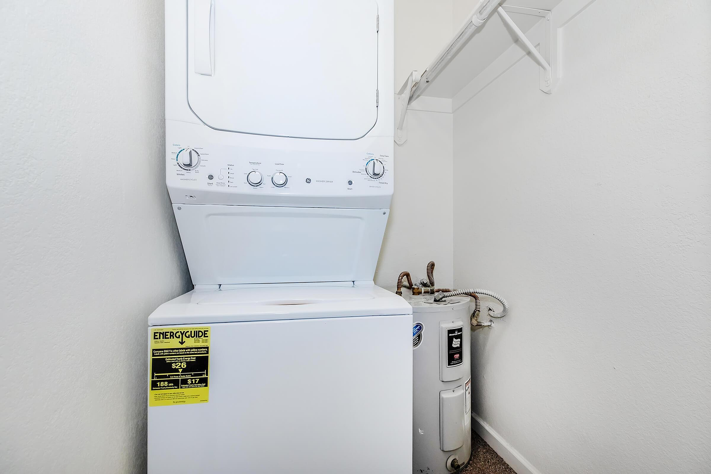 Efficient laundry space featuring a modern stacked washer and dryer set alongside a compact water heater.