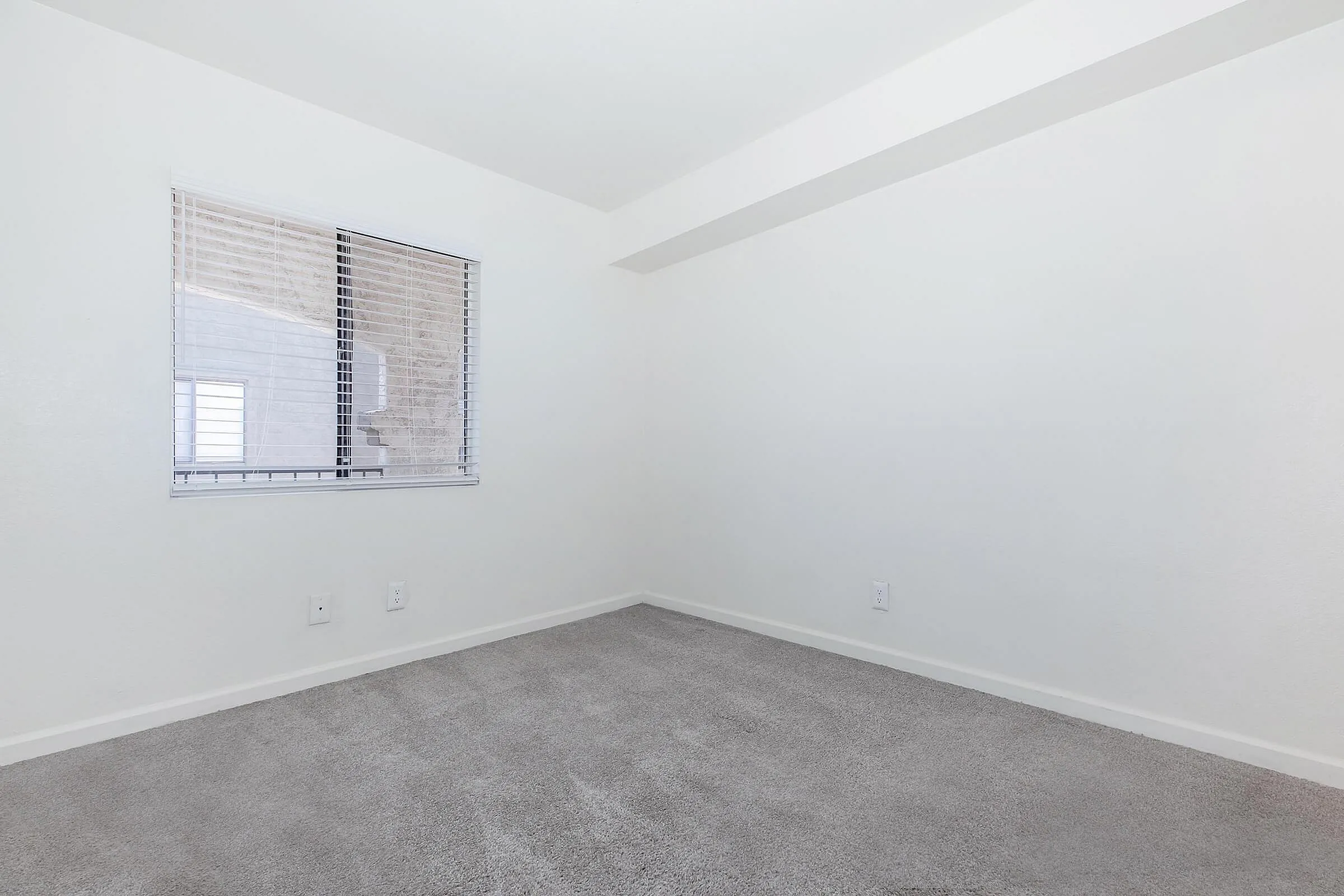 Bright and airy room with plush carpet flooring and a large window letting in natural light, perfect for creating a cozy living space.
