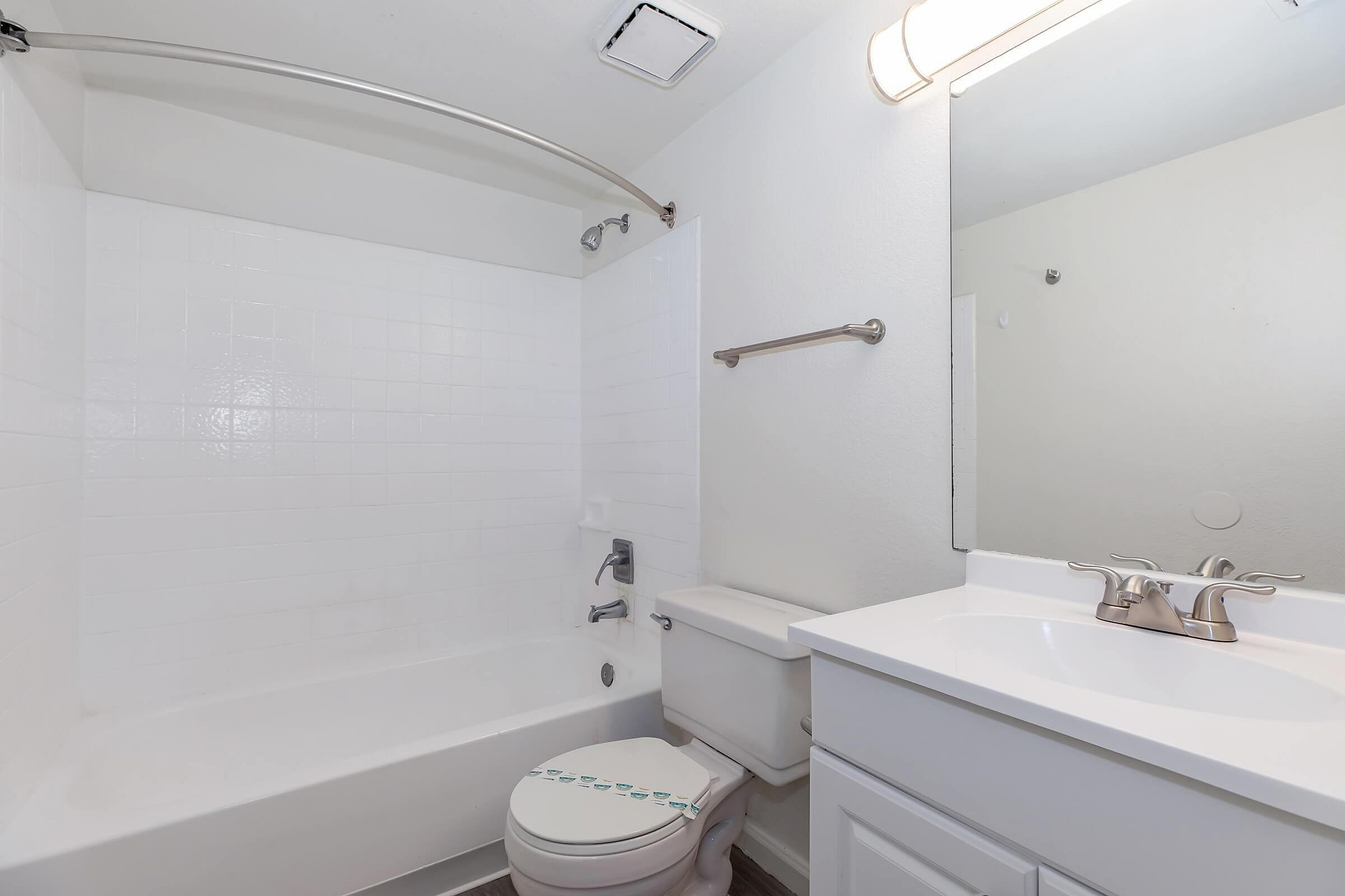 Modern bathroom with sleek white fixtures, a full bathtub, elegant mirror, and bright lighting.