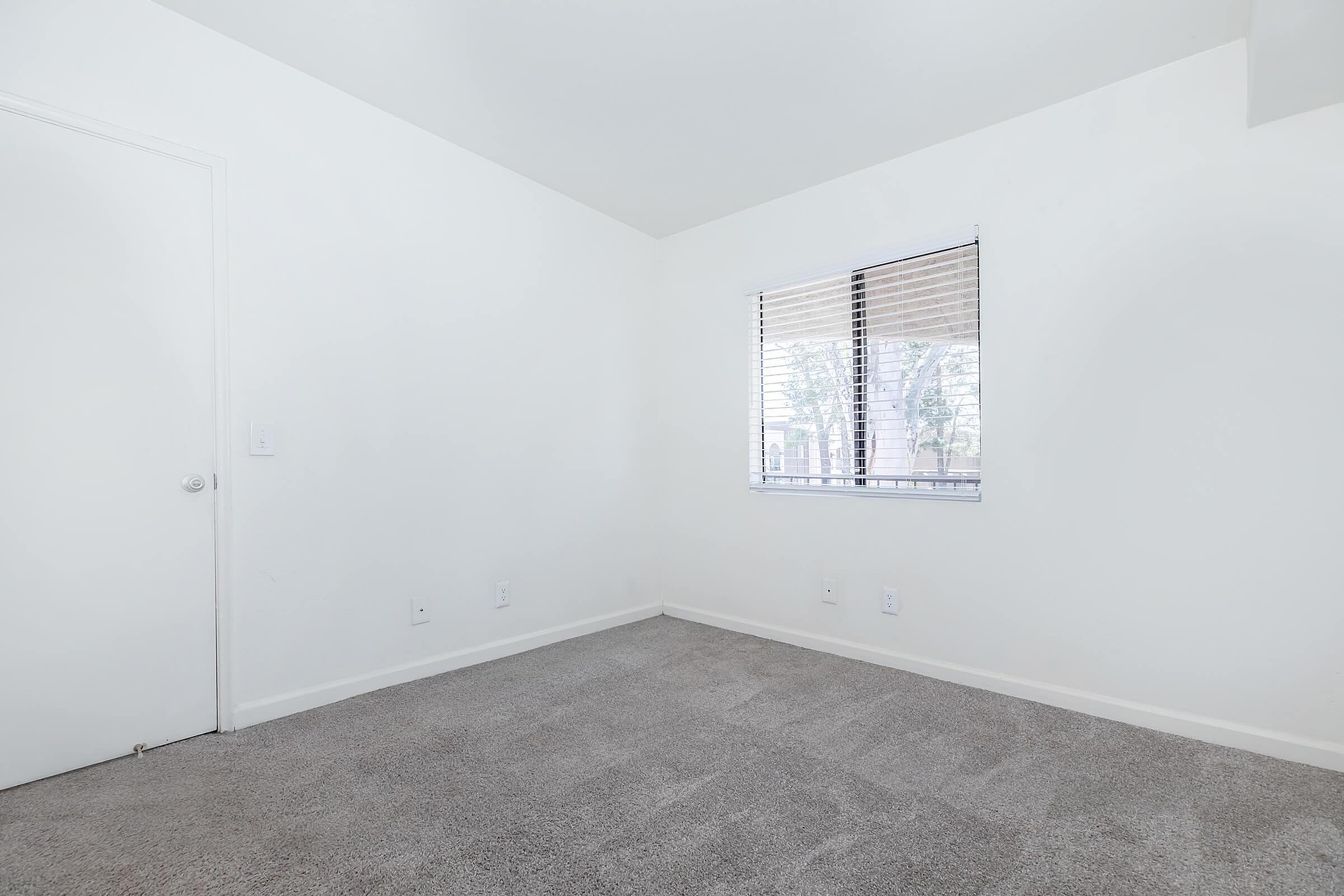 Bright, modern room with neutral carpet, large window with blinds, and crisp white walls offering a fresh canvas for your personal touch.