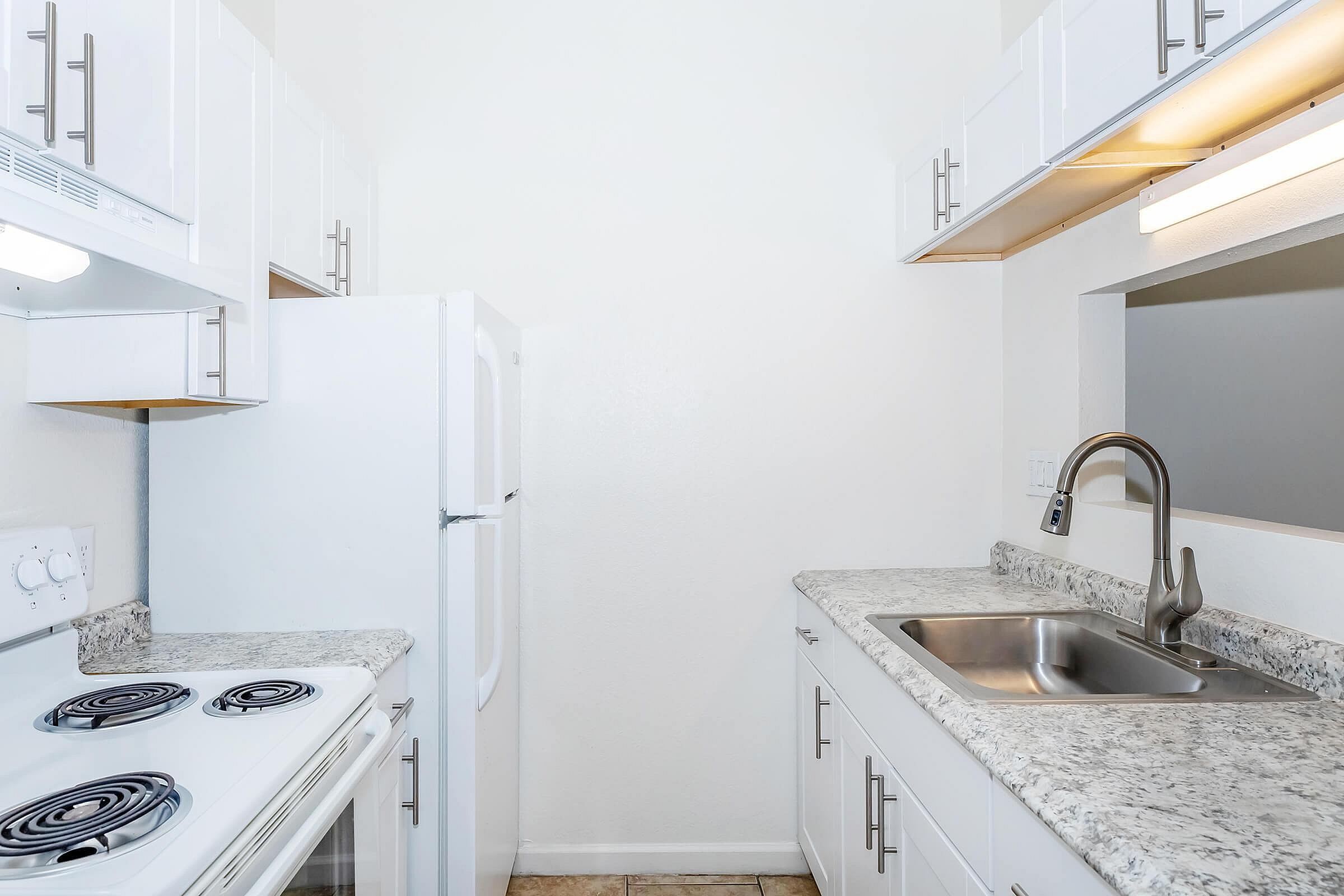 Bright, compact kitchen with modern white cabinetry, sleek granite countertops, and a stainless steel sink, perfect for efficient meal prep.