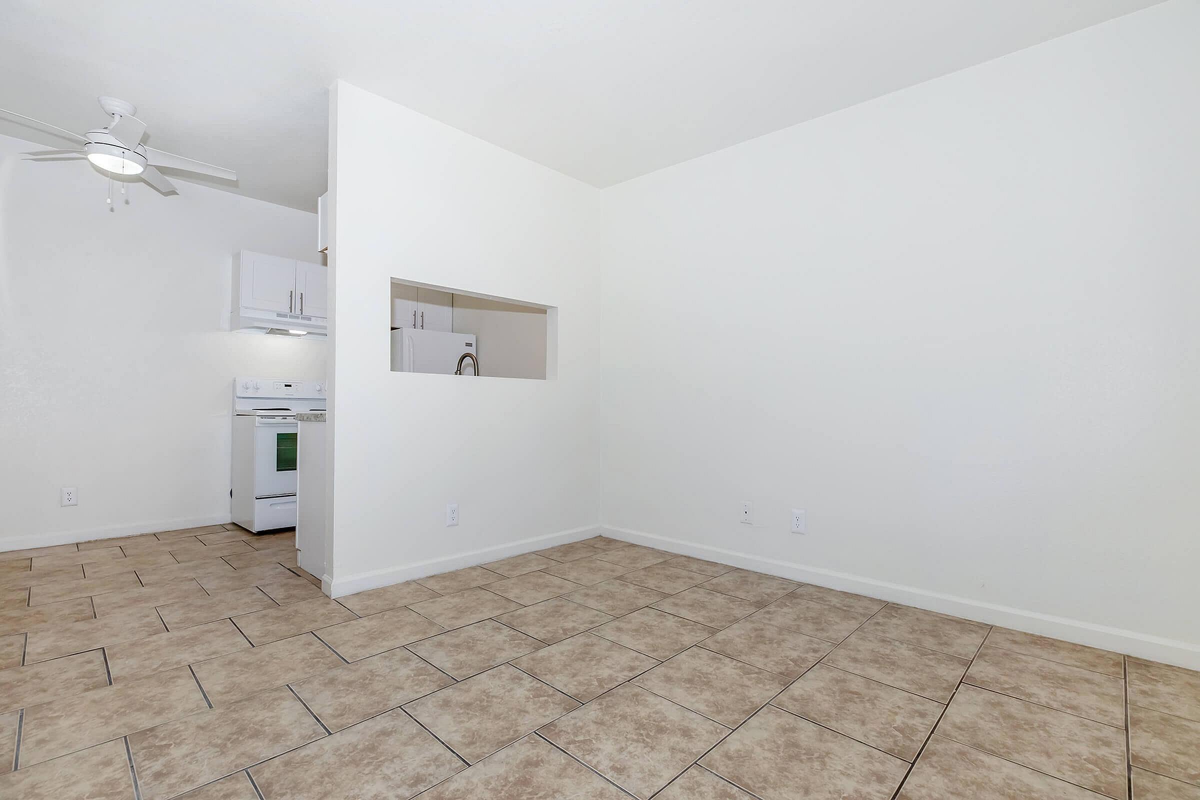 Bright open space with tiled floors, featuring a modern kitchen glimpse and ceiling fan, perfect for comfortable living.