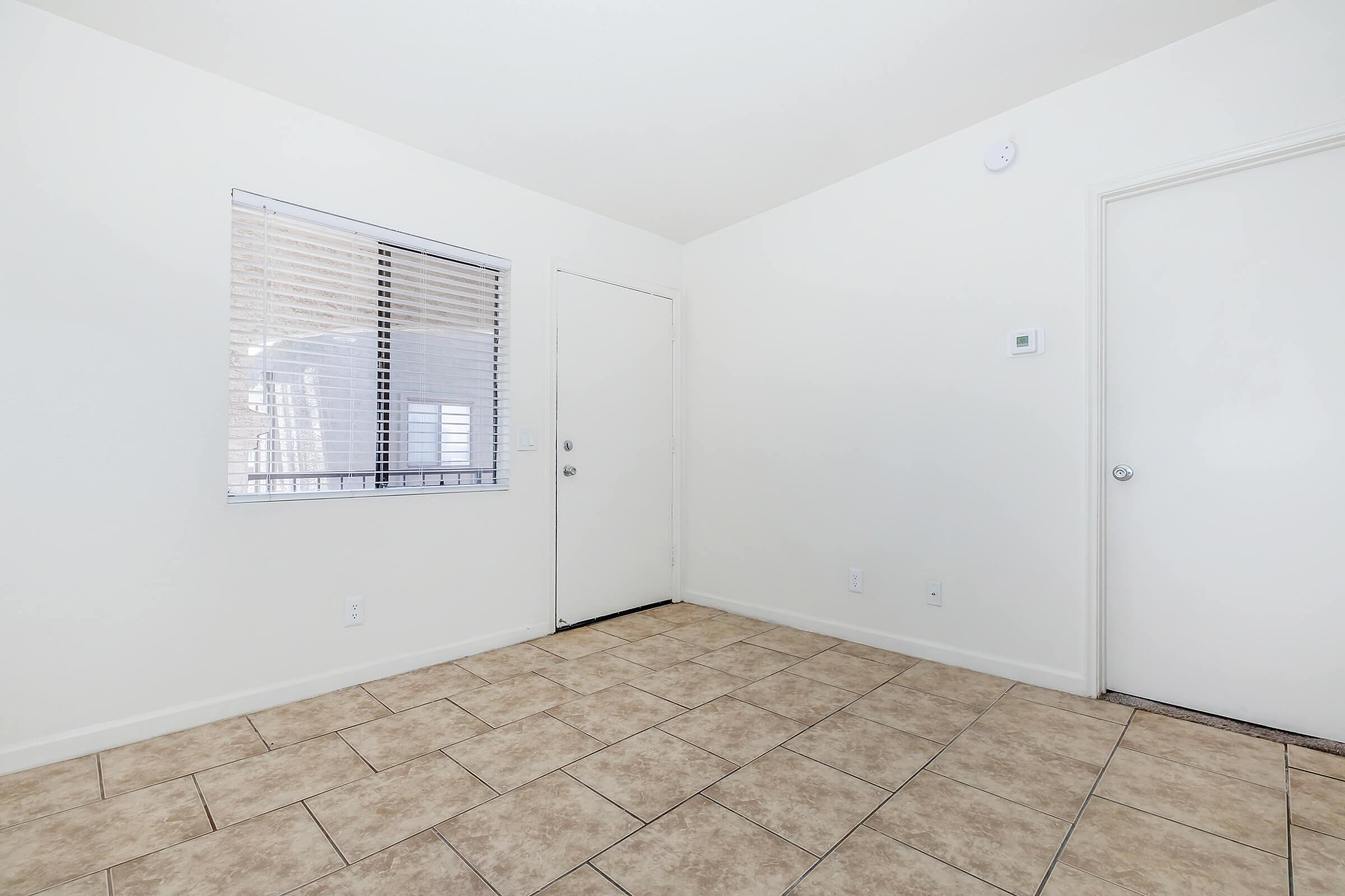 Bright and open apartment space with elegant tiled flooring, pristine white walls, and a large window inviting natural light.