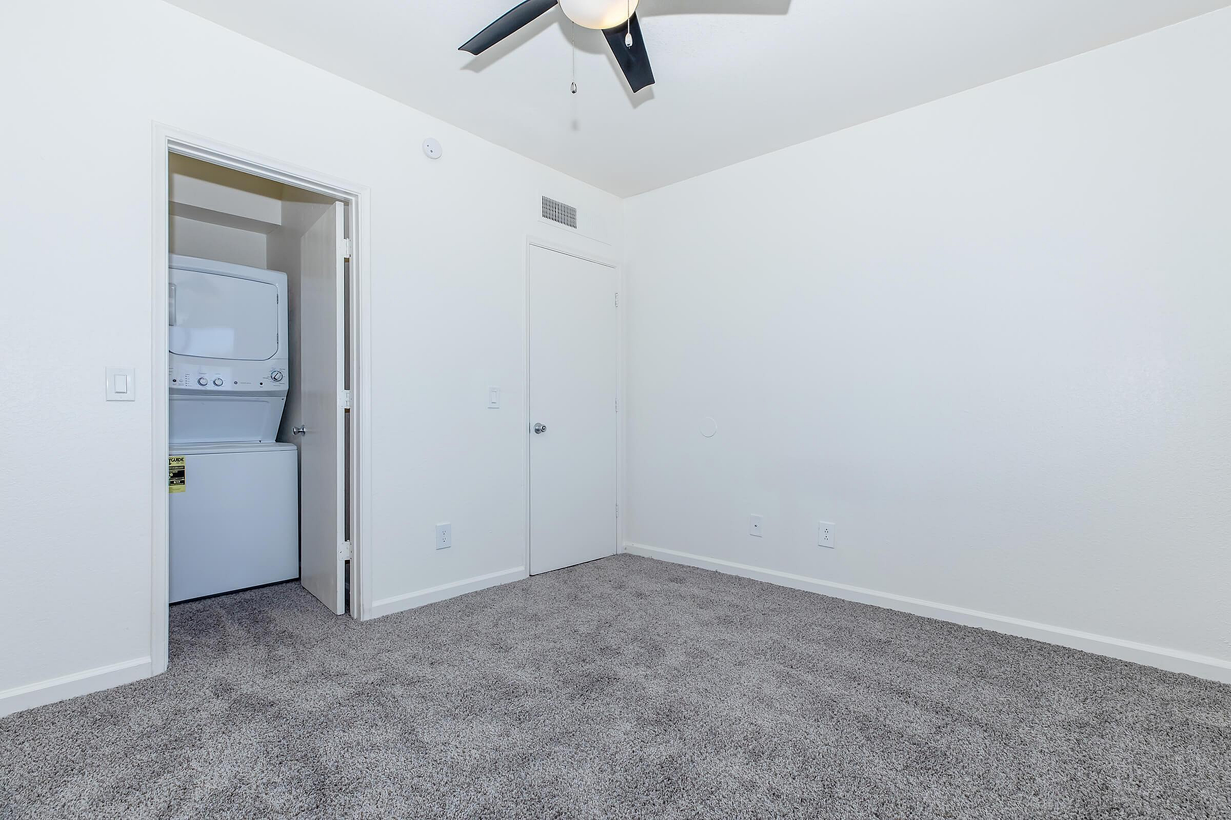 Bright room with plush carpeting and an in-unit washer and dryer, offering modern convenience in a sleek apartment layout.