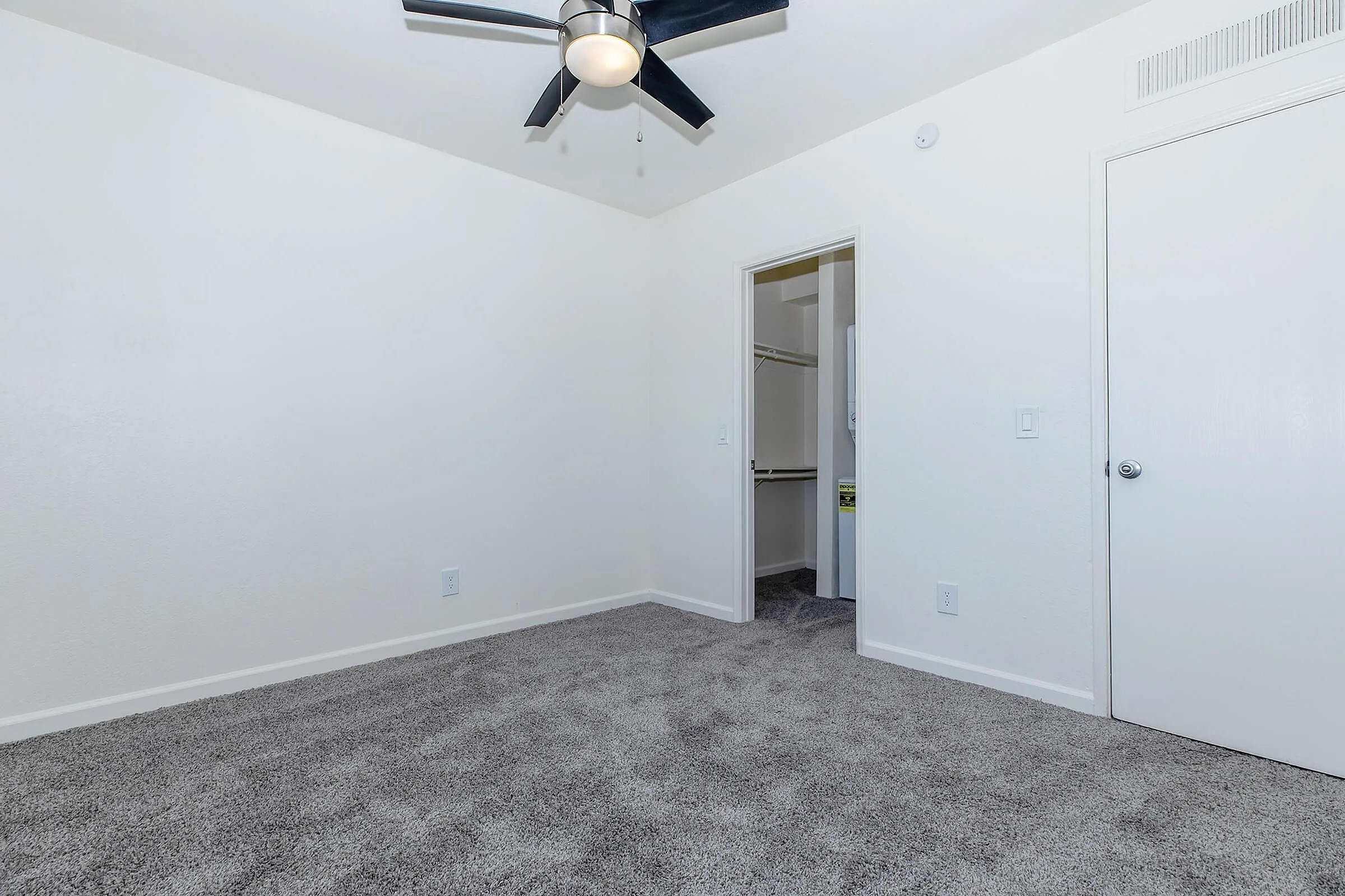 Elegant bedroom featuring plush carpet, modern ceiling fan, and a spacious walk-in closet.