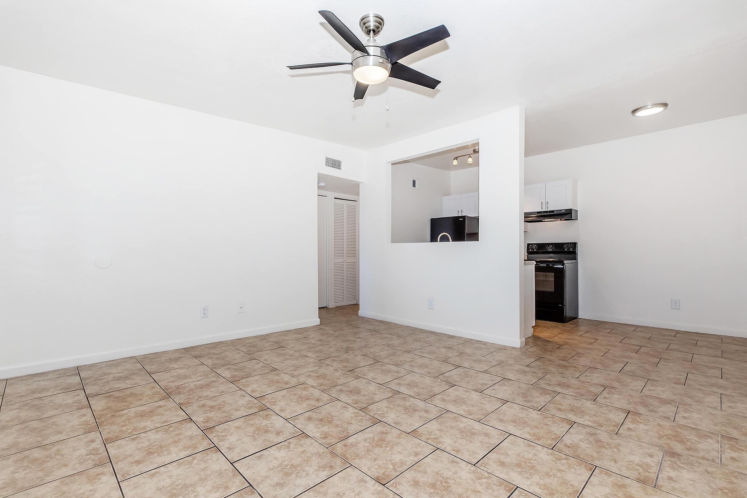 Bright modern living space with sleek ceiling fan, open kitchen view, and elegant tile flooring.