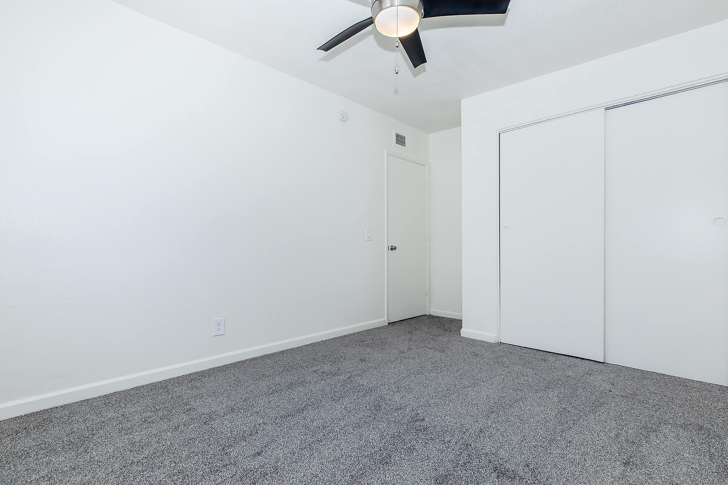 Bright, freshly painted room with plush carpet and modern ceiling fan, perfect for a serene retreat.