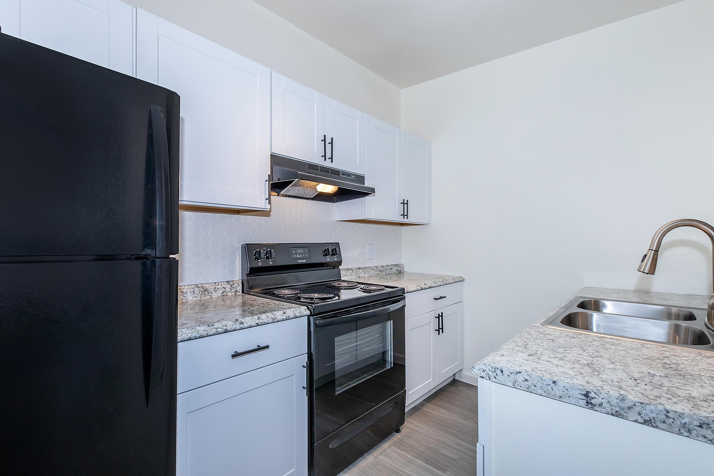 Modern kitchen with sleek black appliances, granite countertops, and white cabinetry.
